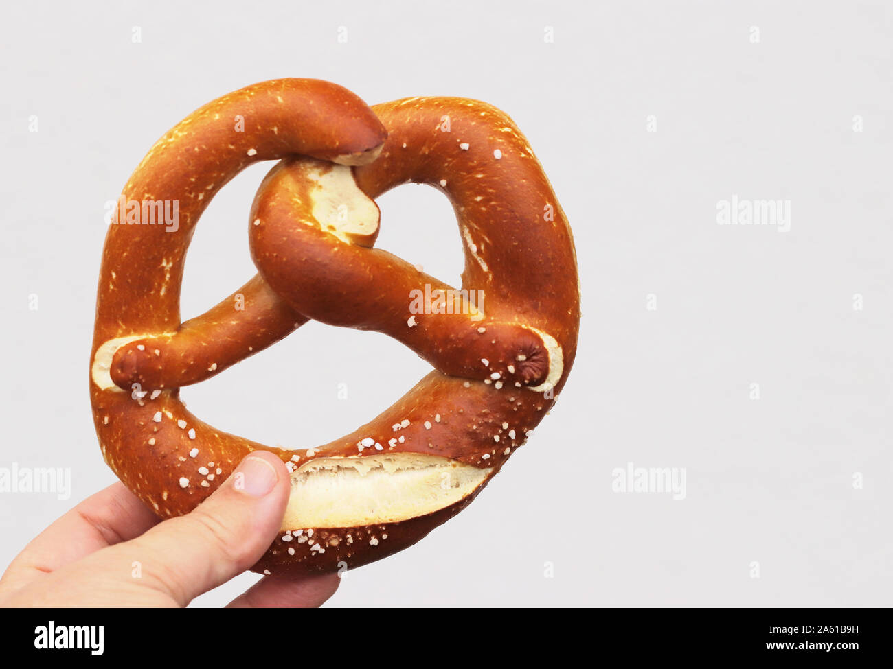 Hand mit einem frisch gebackene Bayerische brezel vor einem hellen Hintergrund mit Kopie Raum Stockfoto