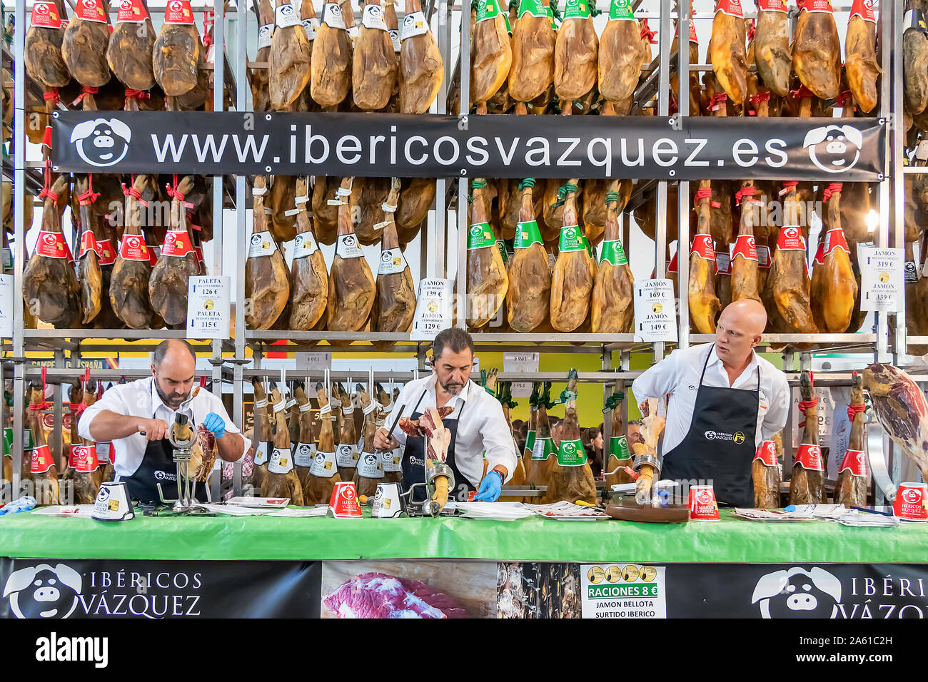 Aracena, Huelva, Spanien - Oktober 20, 2019: Metzger schneiden Scheiben eines spanischen Iberian Serrano Schinken mit einem Aussteller der ausgehärteten Iberico Schinken im Hinterg Stockfoto