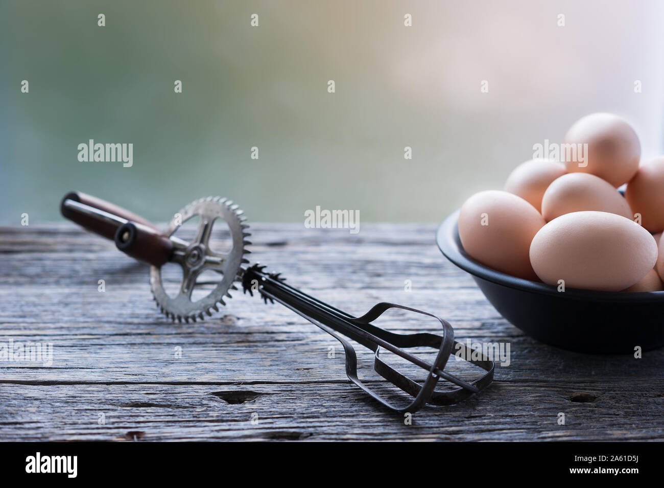 Altes ei Schneebesen Mixer und eine Schüssel mit Bio Eier im rustikalen Holztisch verwitterten grauen Hintergrund. Selektive konzentrieren. Horizontal, mit kopieren. Stockfoto