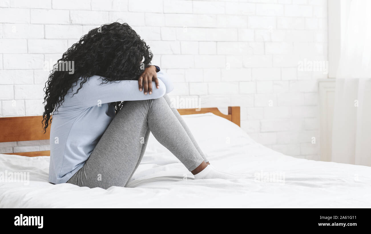 Deprimiert junge Mädchen auf dem Bett sitzen, die Knie umarmt Stockfoto