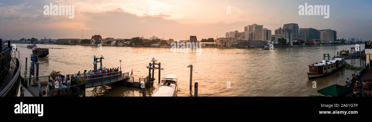 Abendliche Boote gleiten entlang Bangkoks Chao Phraya Fluss und verbinden traditionellen Charme mit der urbanen Skyline der Stadt in einer ruhigen Flussszene. Stockfoto