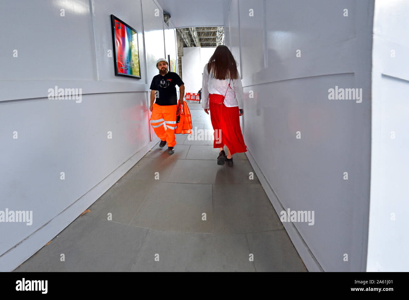 London, England, UK. Junge Frau in Weiß Top und Red Rock gehen unter Gerüste im Aktionsbereich Stockfoto