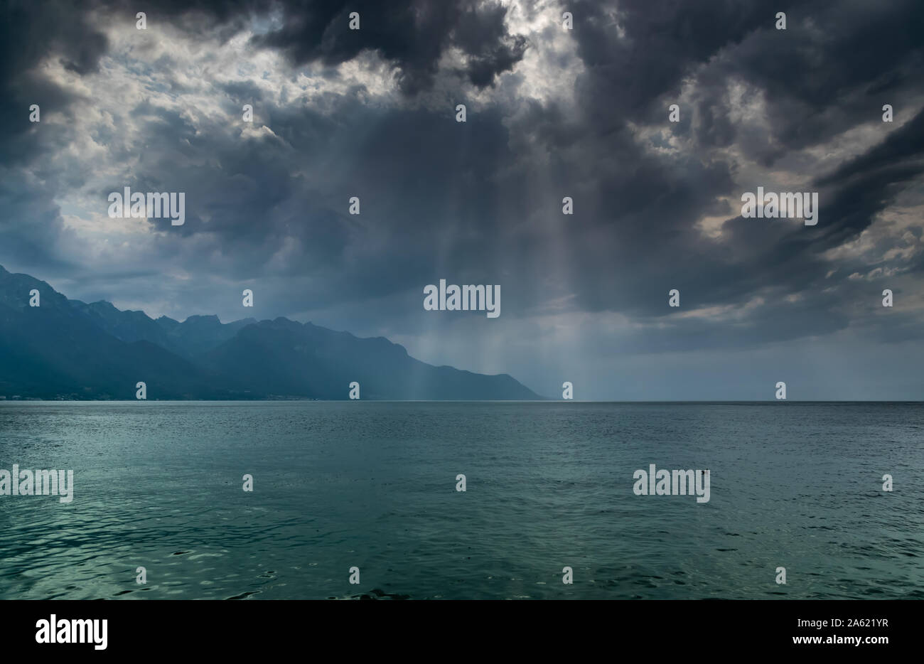 Landschaft der Alpen, Genfer See, dunkle Wolken mit Sonnenstrahlen vor dem Regen. Schuß vom Ufer des Sees in Montreux, Schweiz. Stockfoto