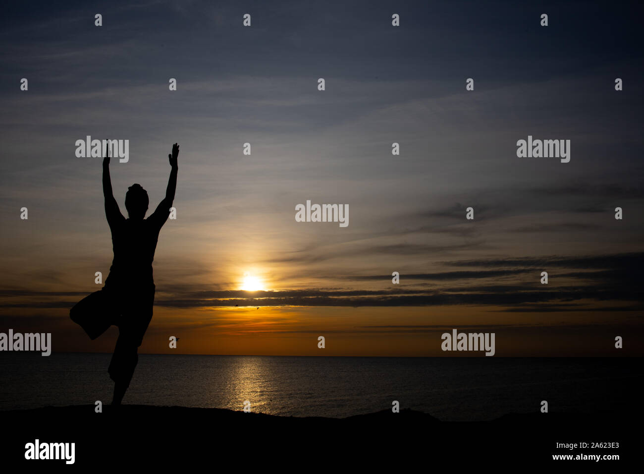 Silhouette einer Frau bei Sonnenuntergang, Yoga Position gegen die untergehende Sonne auf der Insel Bornholm, Dänemark, Yoga bei Sonnenuntergang auf der Insel Stockfoto