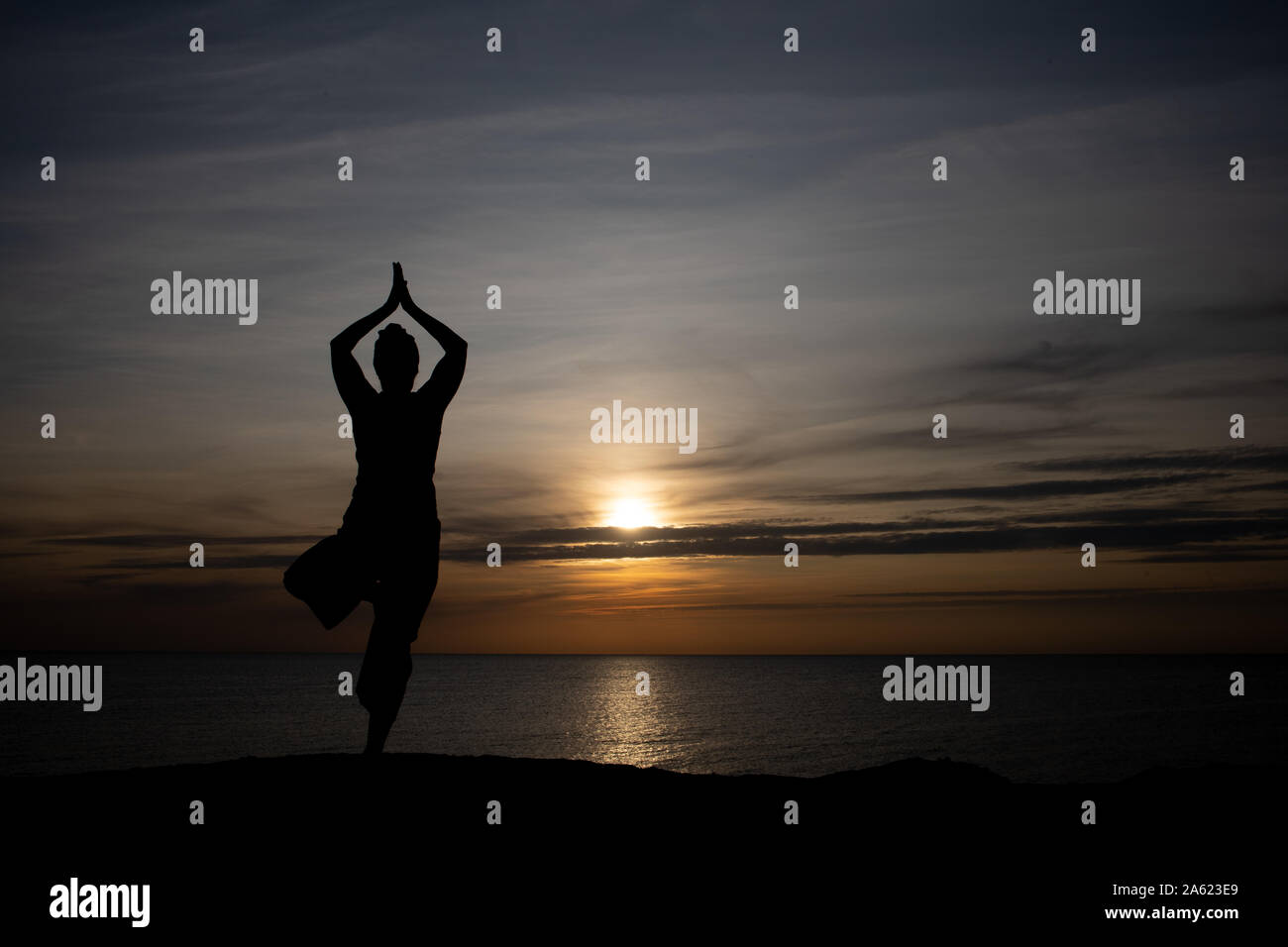 Silhouette einer Frau bei Sonnenuntergang, Yoga Position gegen die untergehende Sonne auf der Insel Bornholm, Dänemark, Yoga bei Sonnenuntergang auf der Insel Stockfoto