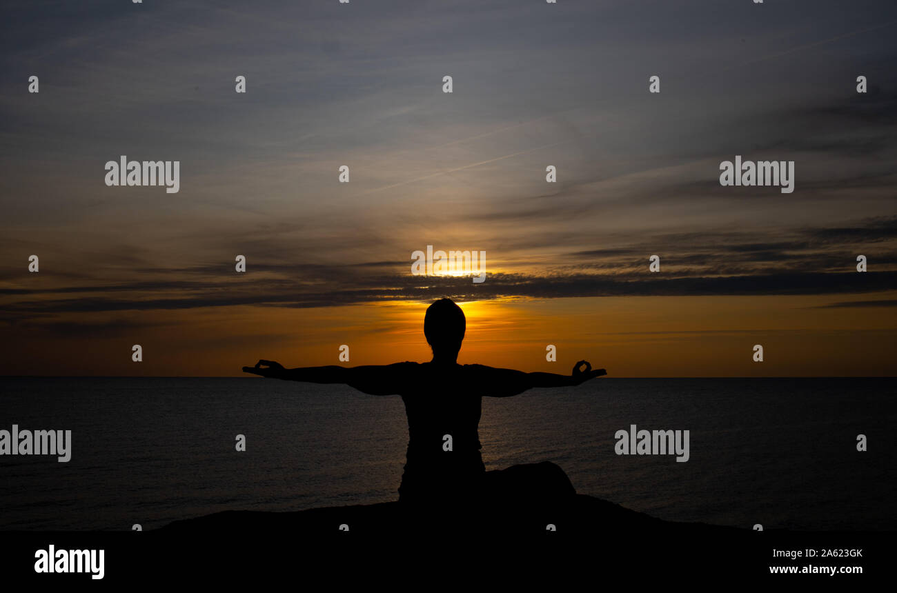 Silhouette einer Frau bei Sonnenuntergang, Yoga Position gegen die untergehende Sonne auf der Insel Bornholm, Dänemark, Yoga bei Sonnenuntergang auf der Insel Stockfoto