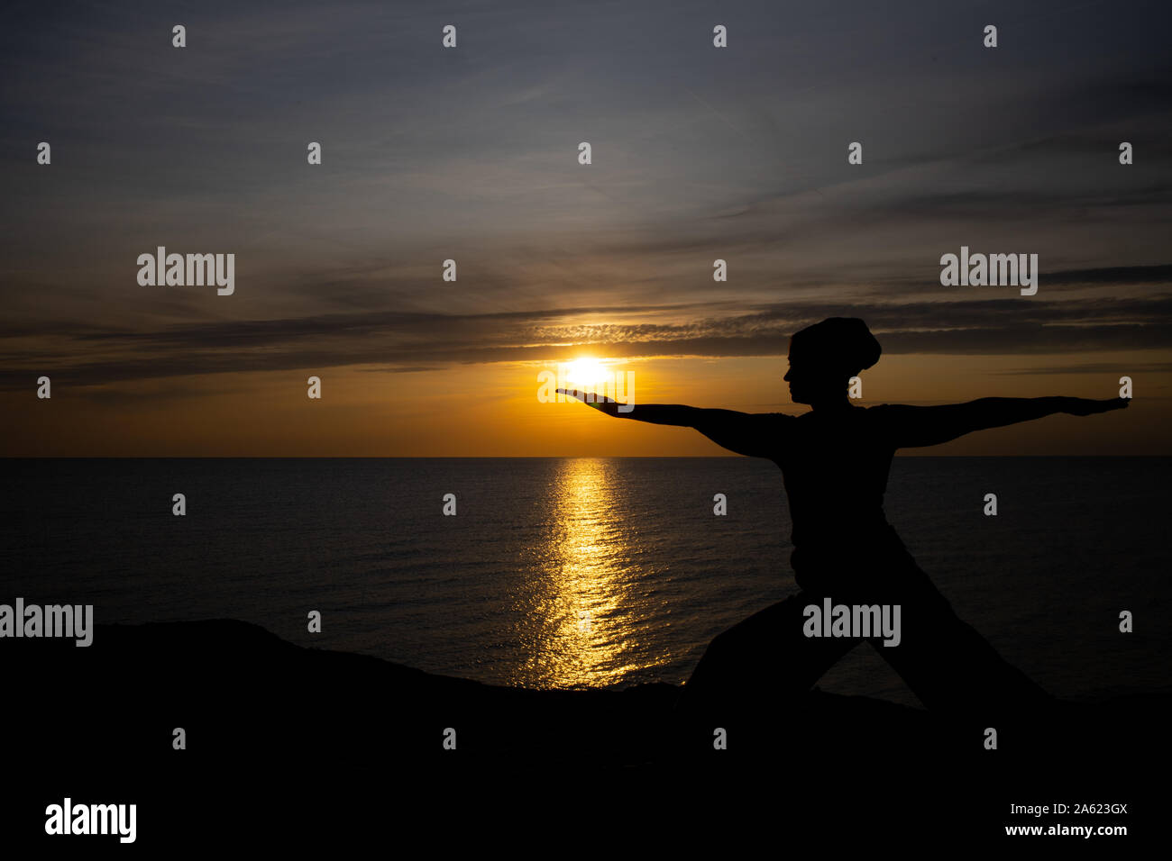 Silhouette einer Frau bei Sonnenuntergang, Yoga Position gegen die untergehende Sonne auf der Insel Bornholm, Dänemark, Yoga bei Sonnenuntergang auf der Insel Stockfoto