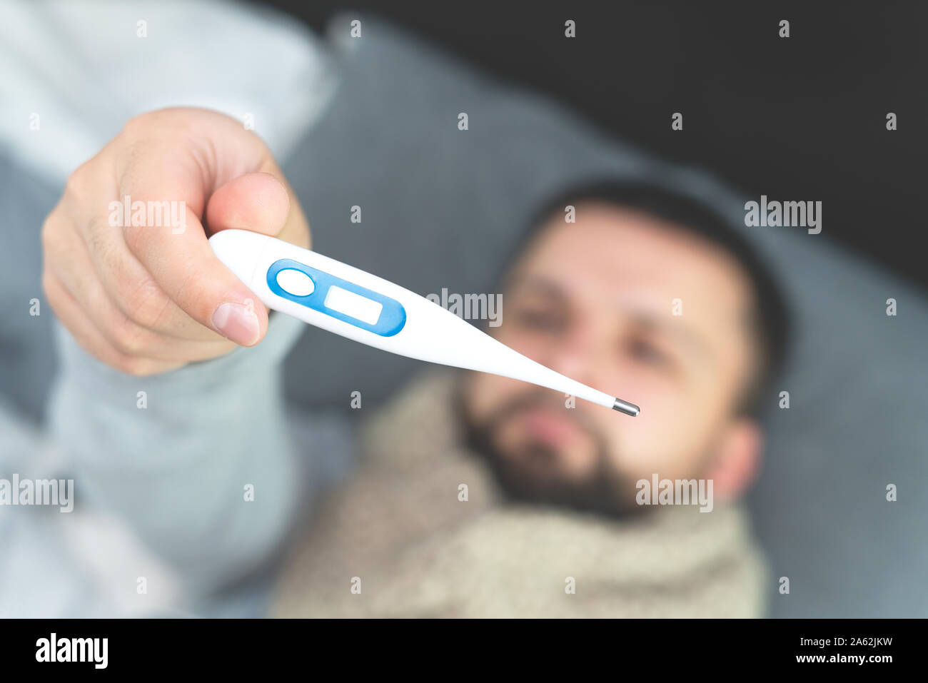Krankheit. Zu Hause erfreuen. Ein junger Mann ist krank, ist zu Hause behandelt. Die Messung der Körpertemperatur. In den Händen eines Mannes ist ein elektronisches Thermometer. Mock Up Stockfoto