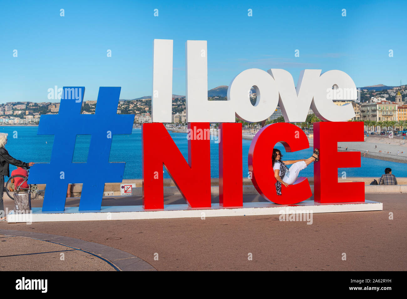 Eine dunkelhaarige Frau touristische stützt auf den Buchstaben "c" in der berühmten Zeichen entlang der Küste der französischen Riviera in Nizza, Frankreich. Stockfoto