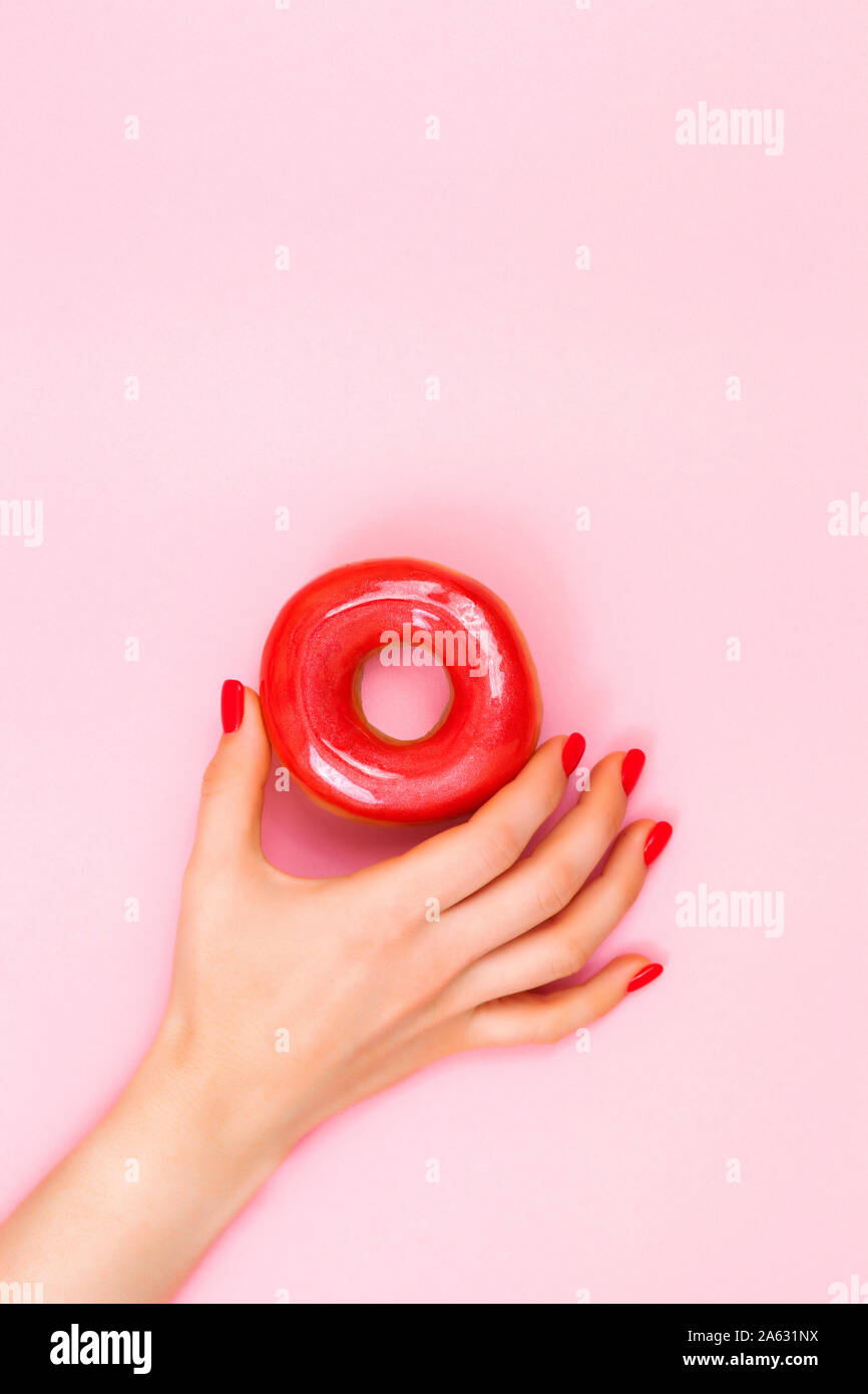 Die schöne junge Frau hand mit perfekte Maniküre halten rot Donut auf rosa Hintergrund. Flach Stil. Stockfoto