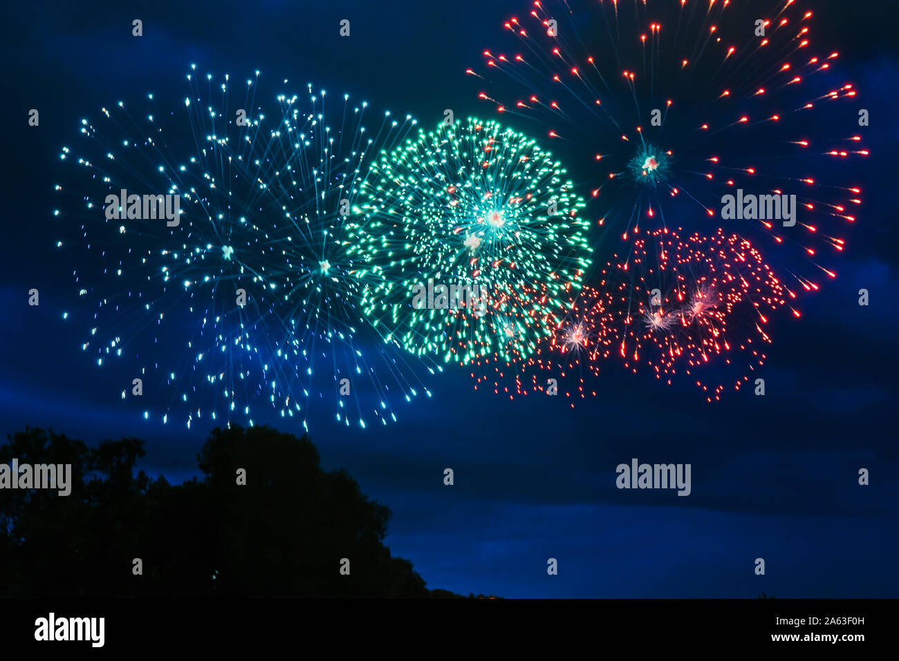 Preiswertes Feuerwerk über der Stadt Rot, Grün und Gelb auf den blauen Himmel. Hell und glänzend. Für jeden Zweck. Feier Konzept. Stockfoto