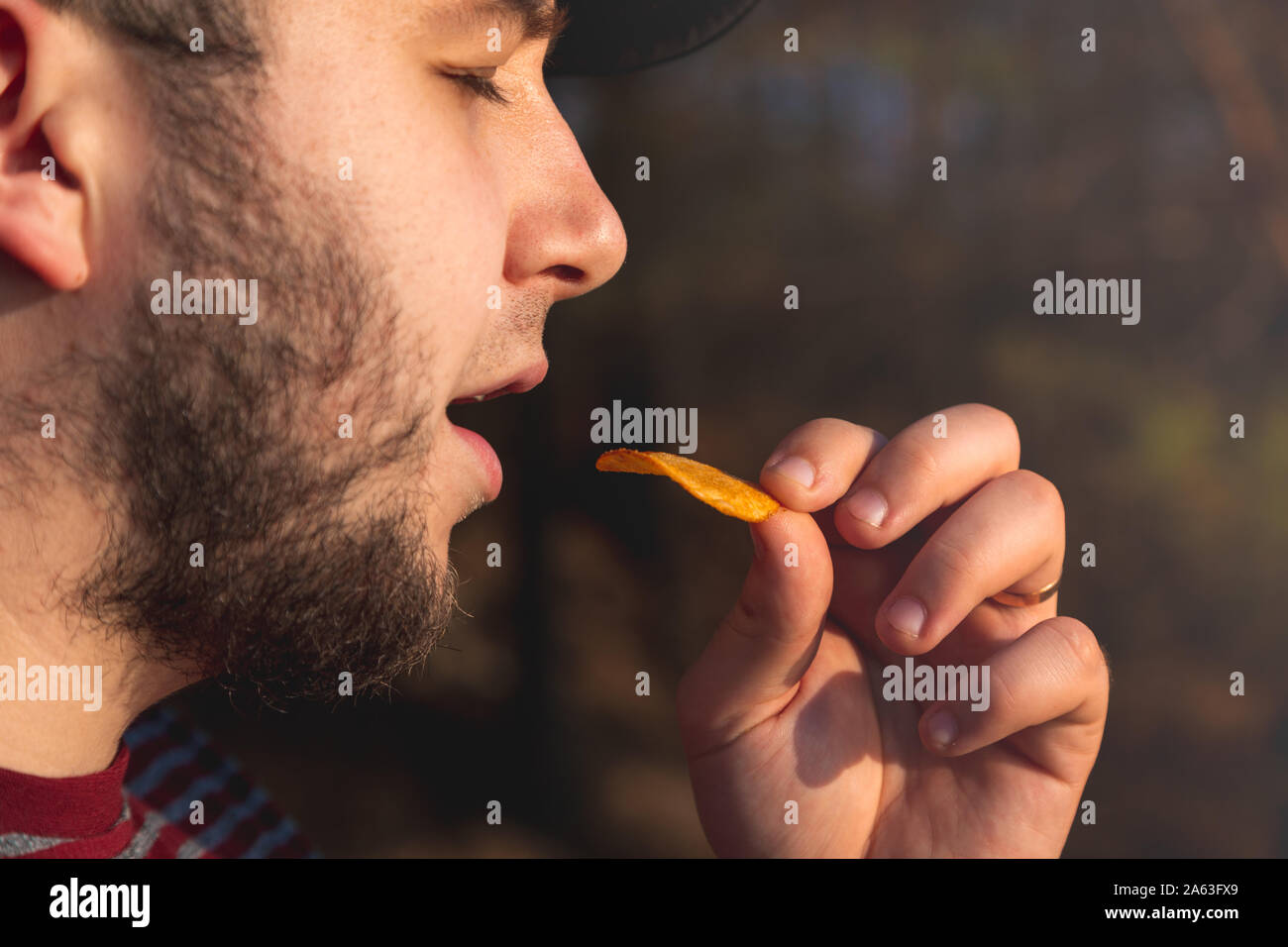Bearder Mann im Wald essen Chips. Im Park Bild im Freien mit unscharfem Hintergrund. Stockfoto