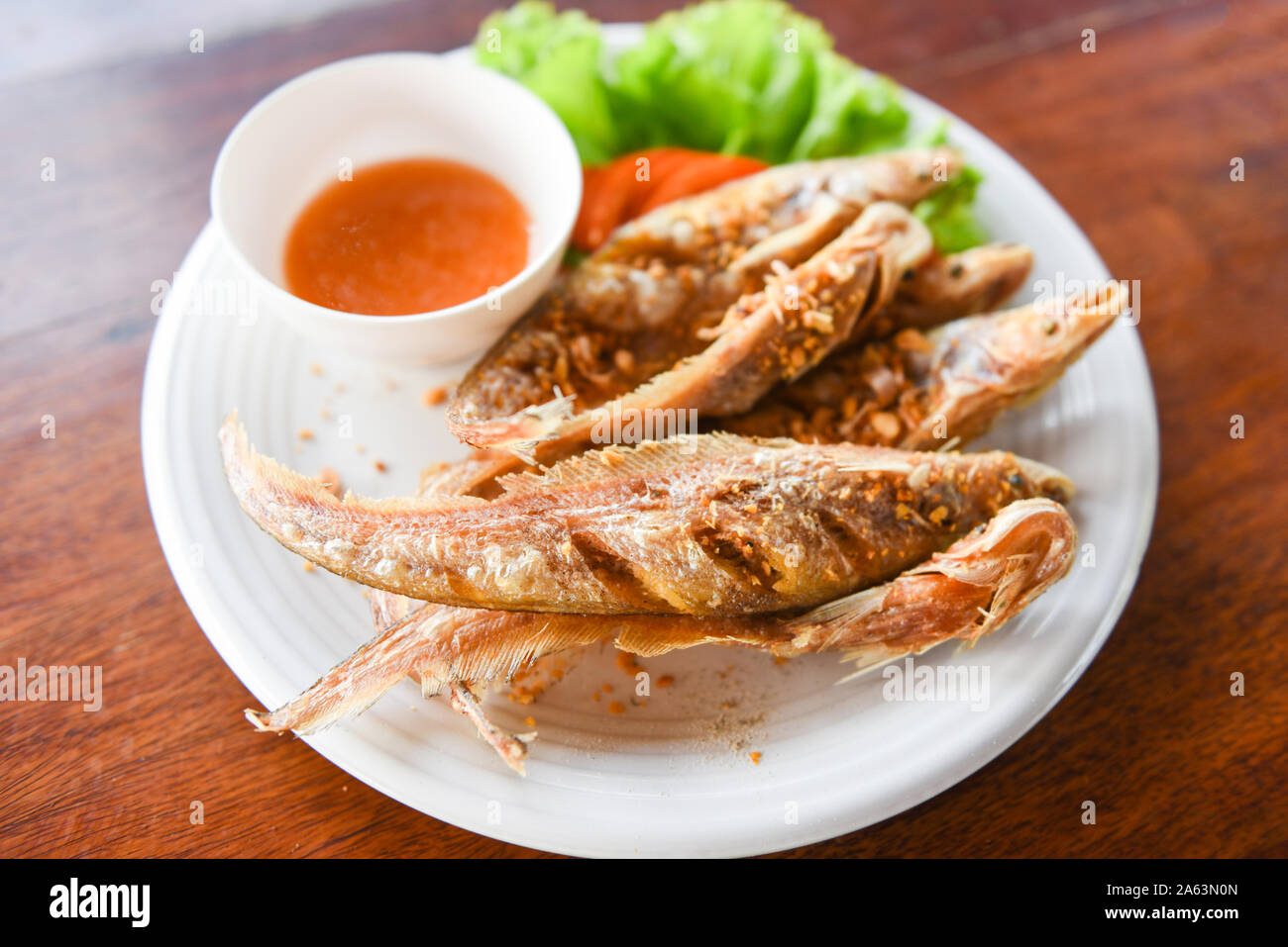 Gebratener Fisch mit Gemüse Salat Tomaten und Soße auf weiße Platte Holztisch/Süßwasserfische Mekong Andere Namen Sheatfishes Siluriformes Silur Stockfoto