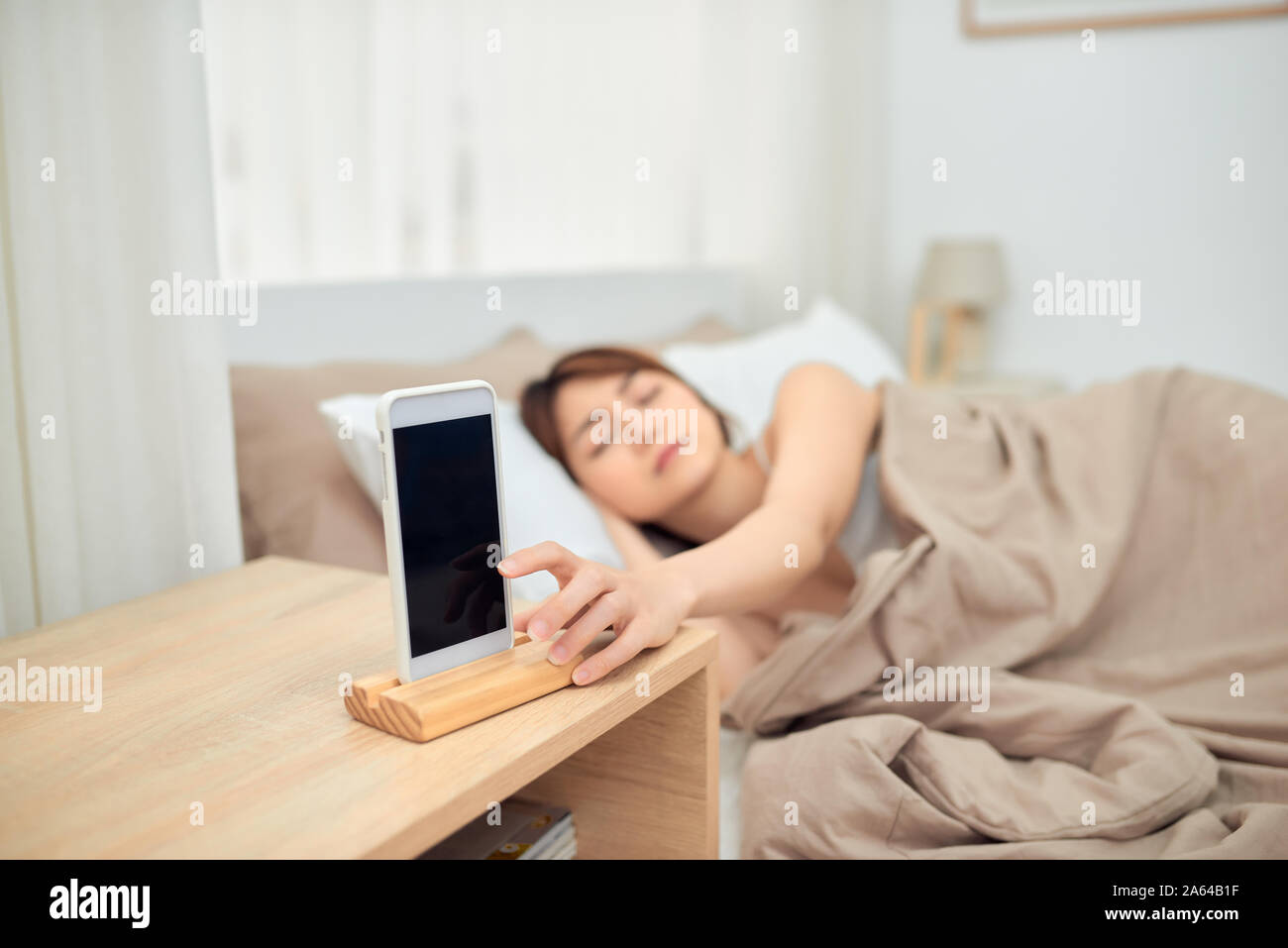 Ärgerlich Alarm. Frau im Bett liegend per Handy geweckt werden, das Ausschalten verrauschtes Signal, Nahaufnahme Stockfoto