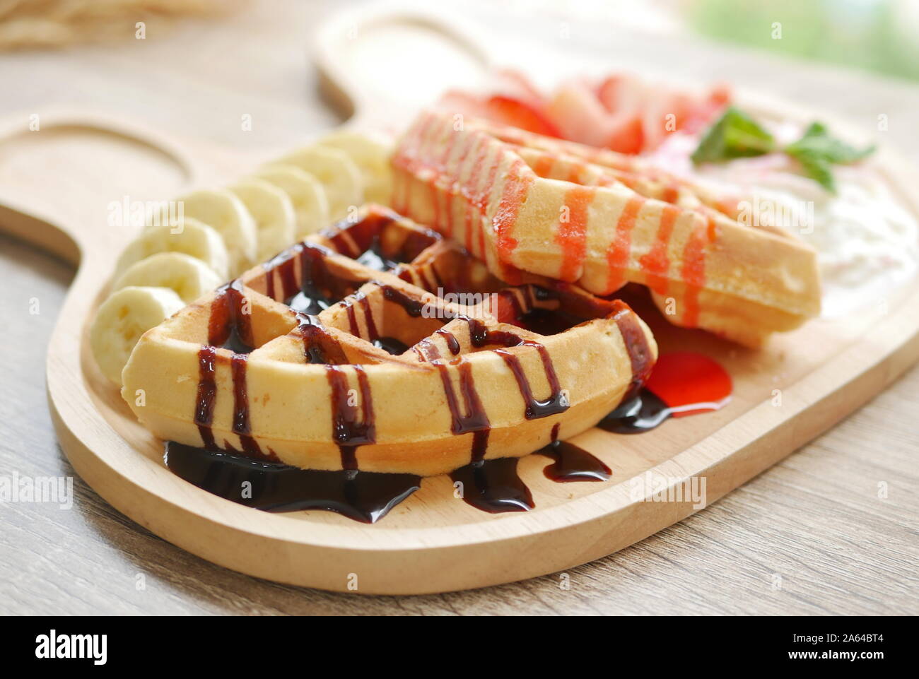 Leckere Waffel garniert mit Erdbeer Sirup und Schokoladensauce, Beilagen sind frische Erdbeere gehackt, Banane, Sahne und Eis serviert. Stockfoto