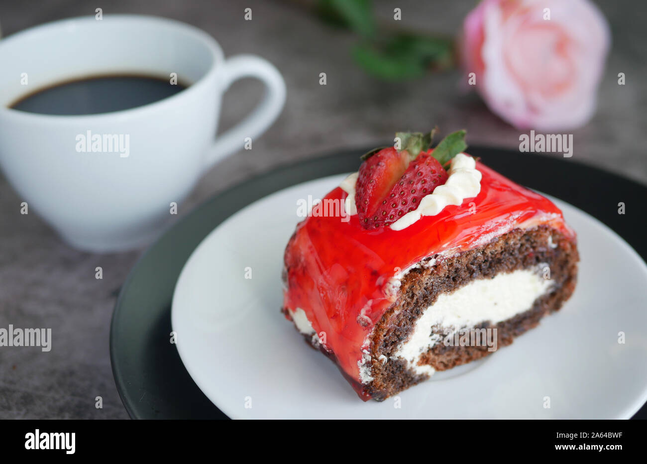 Schokoladenkuchen mit Erdbeermarmelade Sauce garniert mit Schlagsahne und frischen Erdbeeren gehackt auf weiße Platte mit einer Tasse schwarzen Kaffee serviert, blur Stockfoto