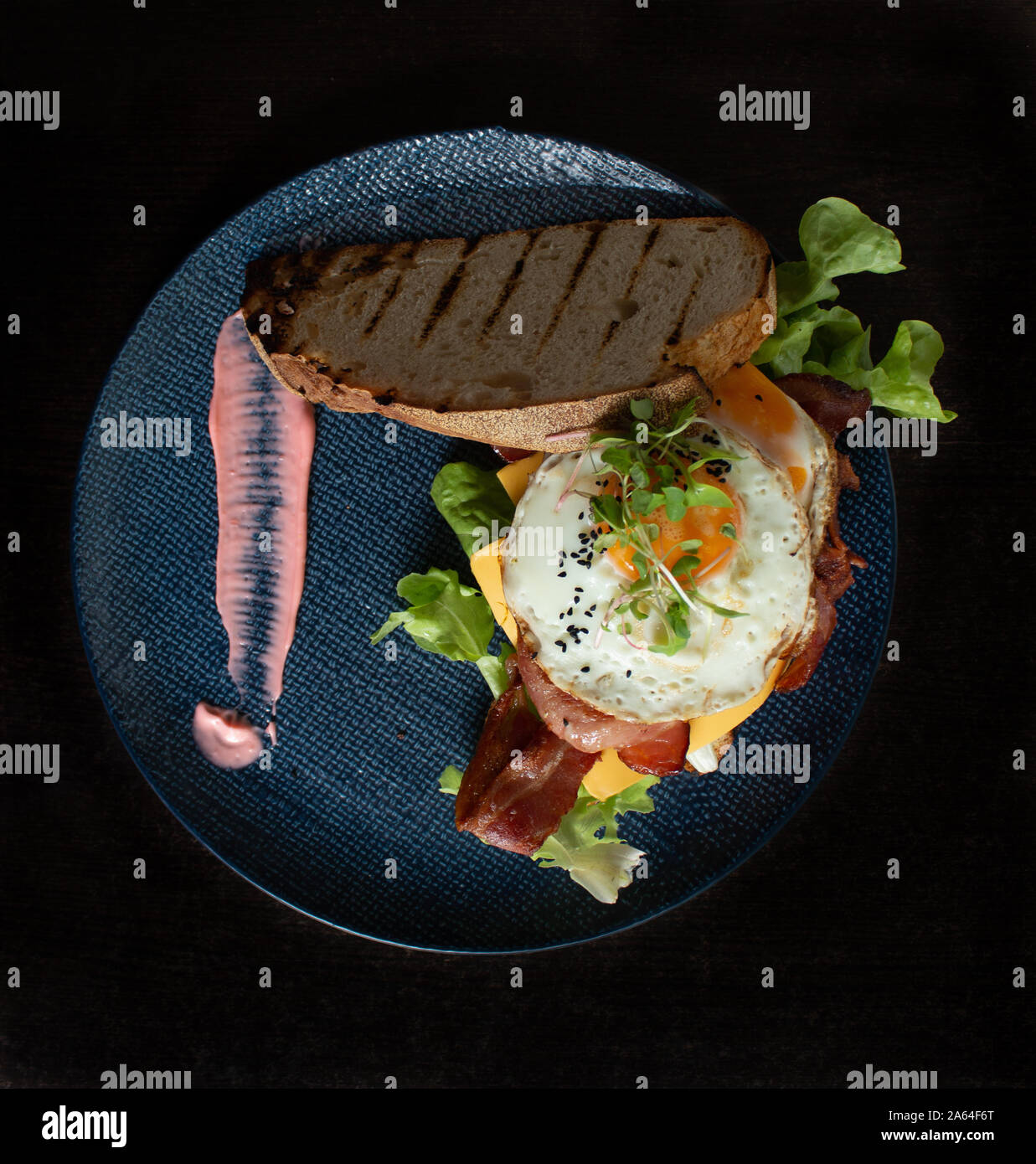 Spiegeleier mit Speck Käse Salat Brötchen Frühstück serviert auf blauen Platte Stockfoto