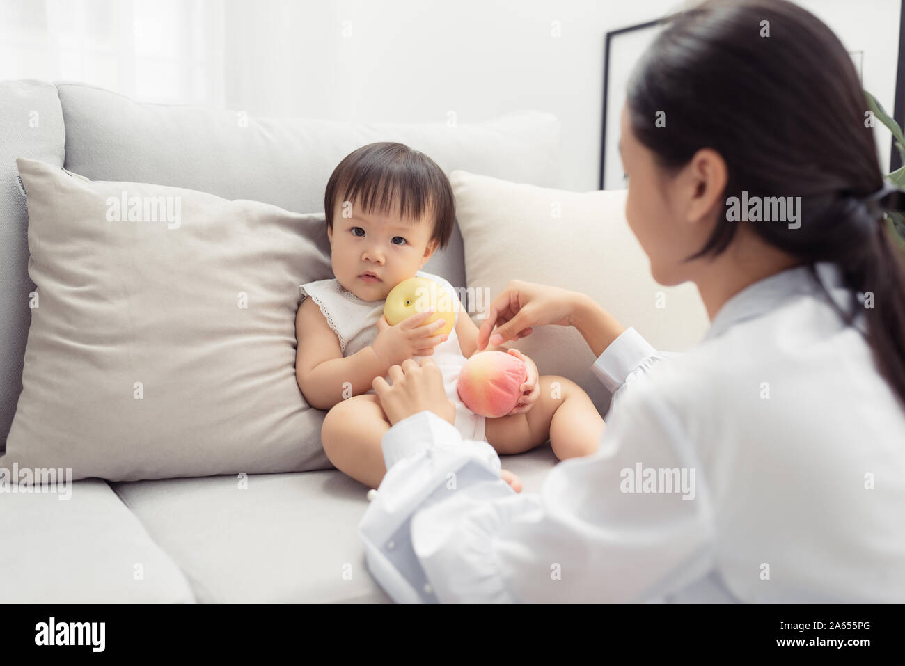 Mama spielt mit ihrer kleinen Tochter auf dem Sofa im Wohnzimmer. Stockfoto