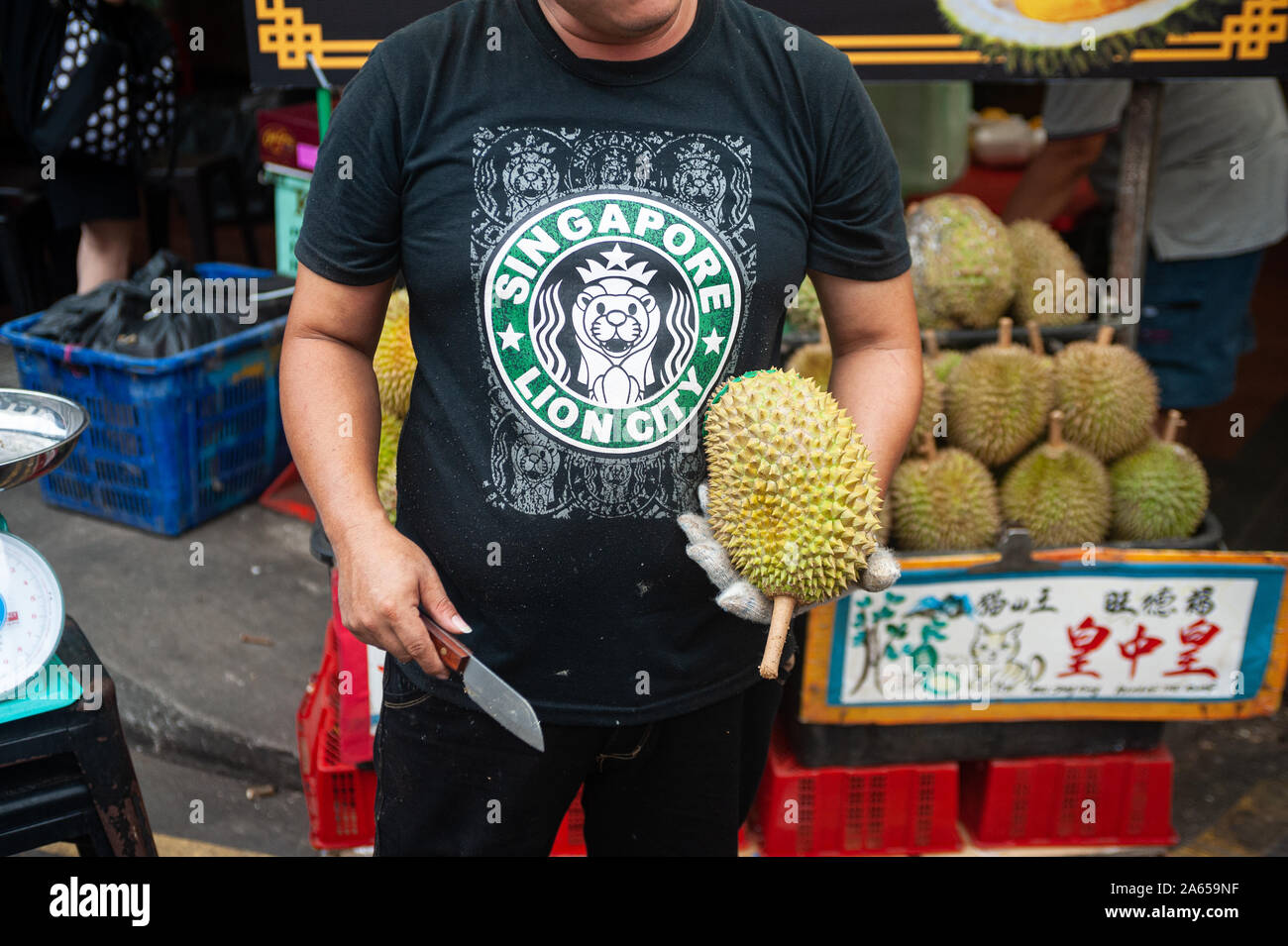 24.02.2019, Singapur, Republik Singapur, Asien - ein Anbieter hält eine frische Durian und ein Messer in der Hand auf einem Straßenmarkt in Chinatown. Stockfoto