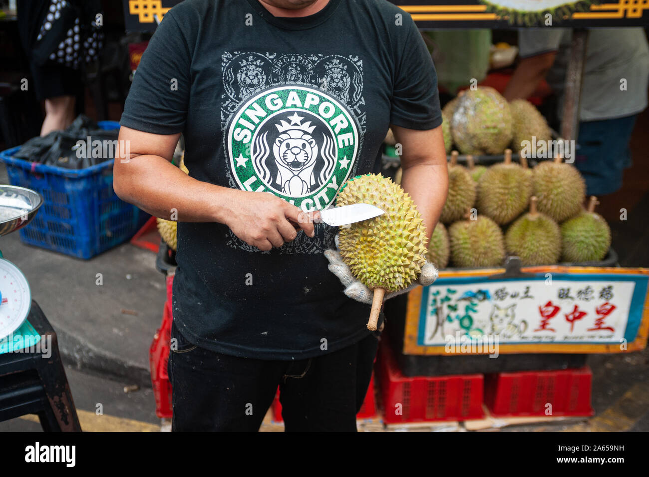 24.02.2019, Singapur, Republik Singapur, Asien - ein Anbieter hält eine frische Durian und ein Messer in der Hand auf einem Straßenmarkt in Chinatown. Stockfoto