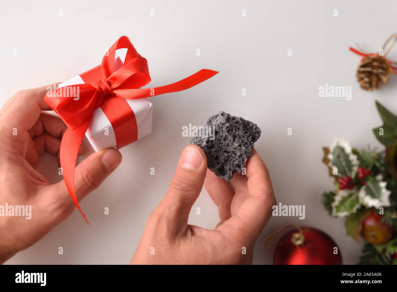 Hände mit Geschenk und Kohle am Weihnachtstag. Konzept für gutes oder schlechtes Verhalten zu belohnen. Horizontale Komposition. Ansicht von oben. Stockfoto