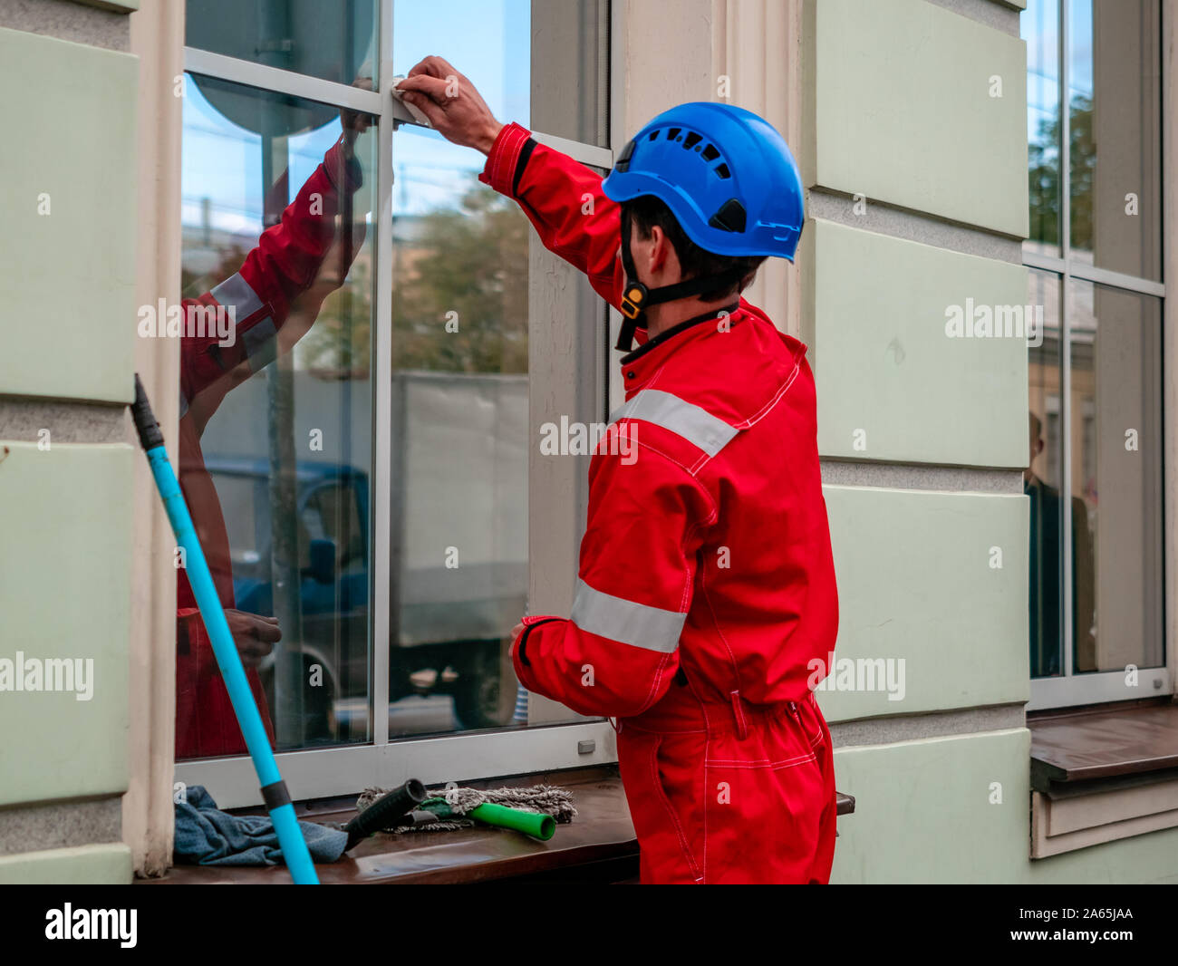 Reiniger mit Mop und Zubehör bereitet Windows in historischer Architektur Gebäude zu waschen. Arbeiter in der Eingebrannten roten Overall, Helm und spezielle equ Stockfoto