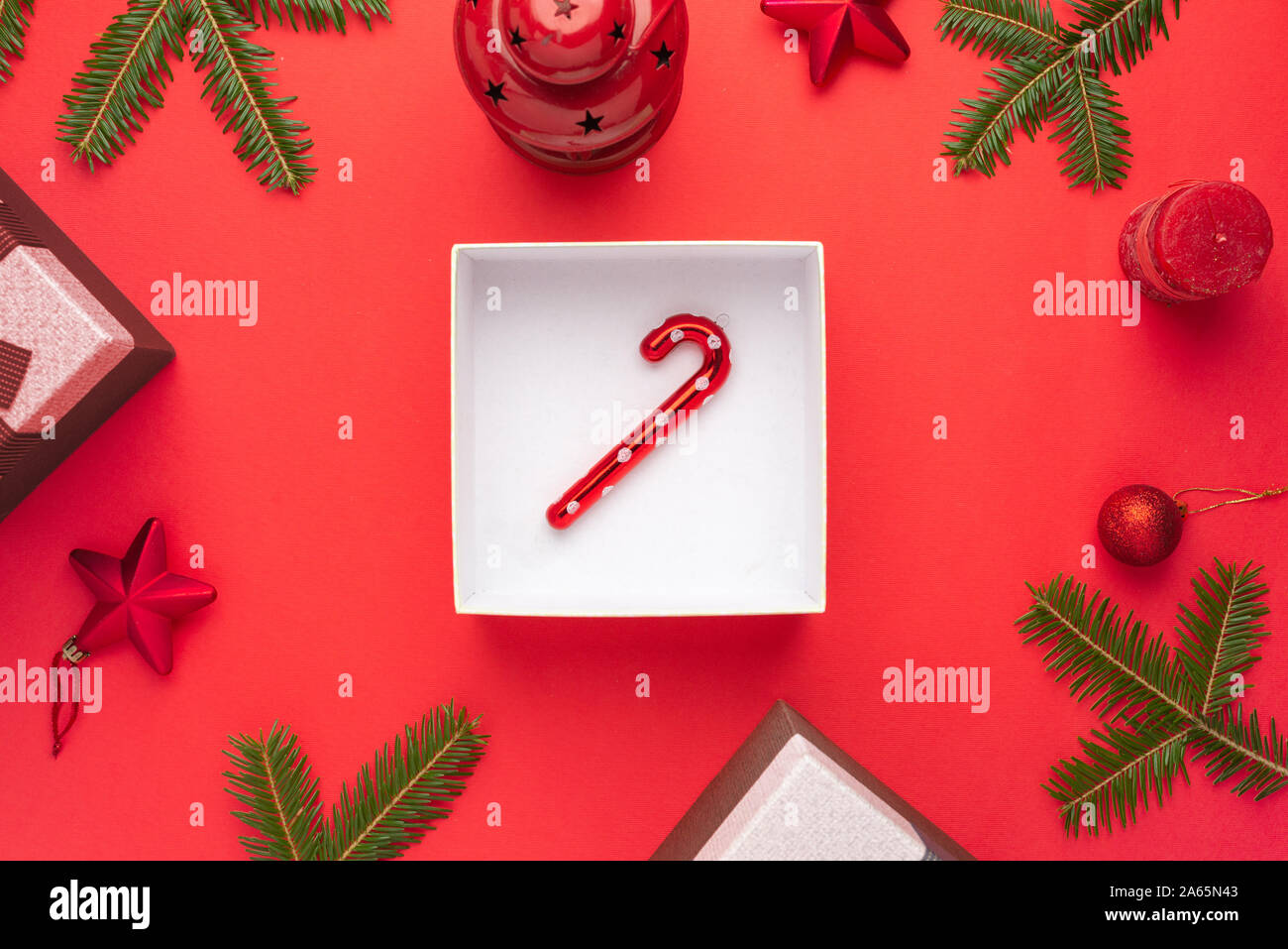 Lollipop in Geschenkbox von Weihnachtsschmuck auf rote Fläche umgeben. Flach, Ansicht von oben. Stockfoto