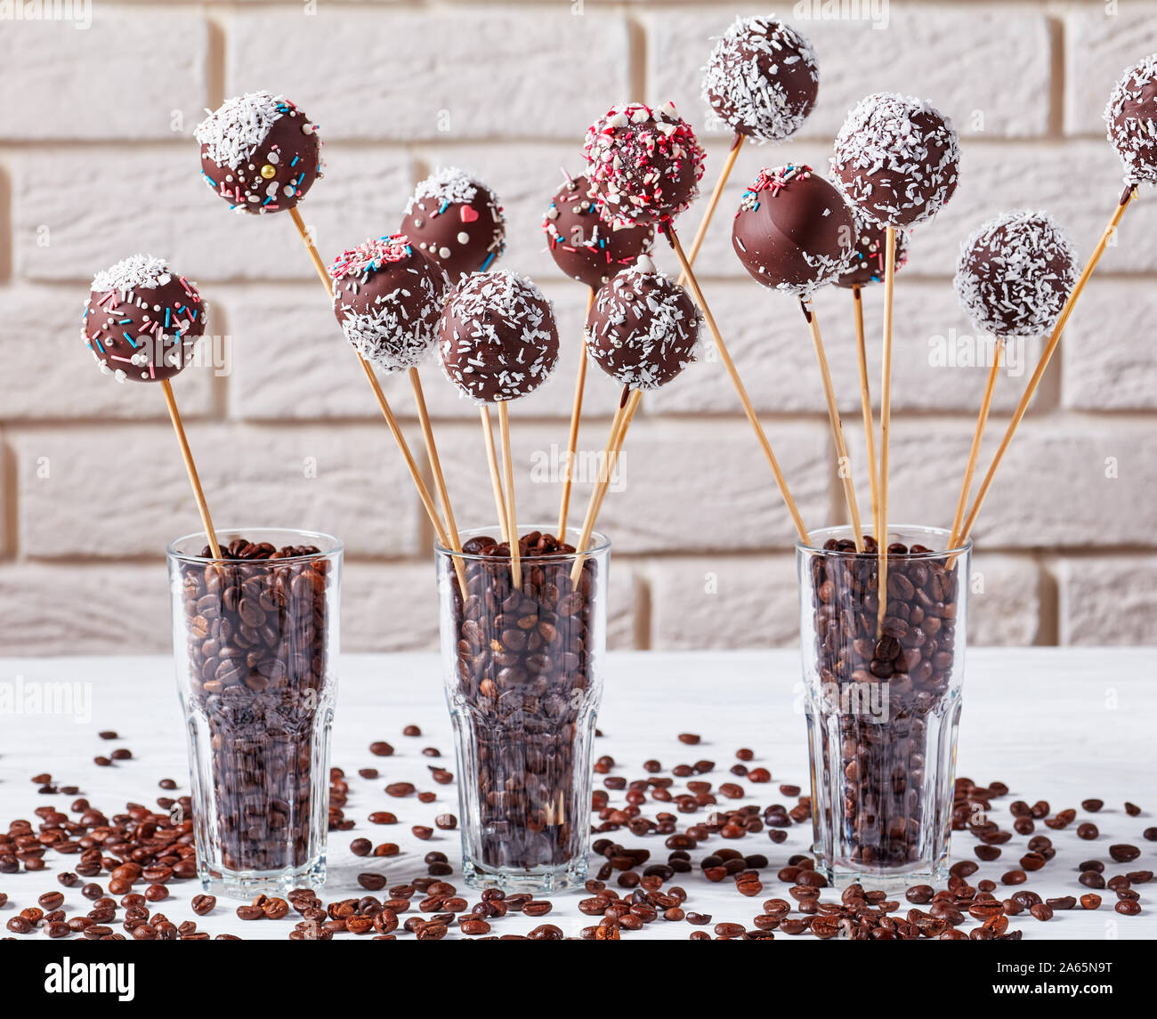 Hausgemachte Schokolade Kuchen pops bestreut mit zerquetschten Bonbons und  Kokosnuss Gitterboxen sollten in drei Gläser mit Kaffee Körner auf einer  konkreten Tabelle. Licht brick Stockfotografie - Alamy