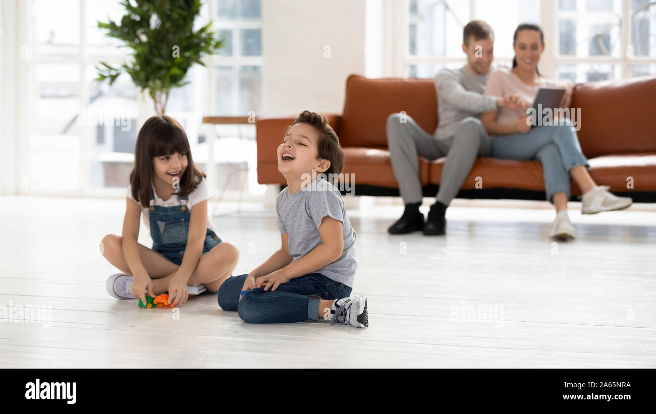 Fröhliche Geschwister mit Spielzeug, zusammen zu spielen, Eltern sitzen auf der Couch. Stockfoto