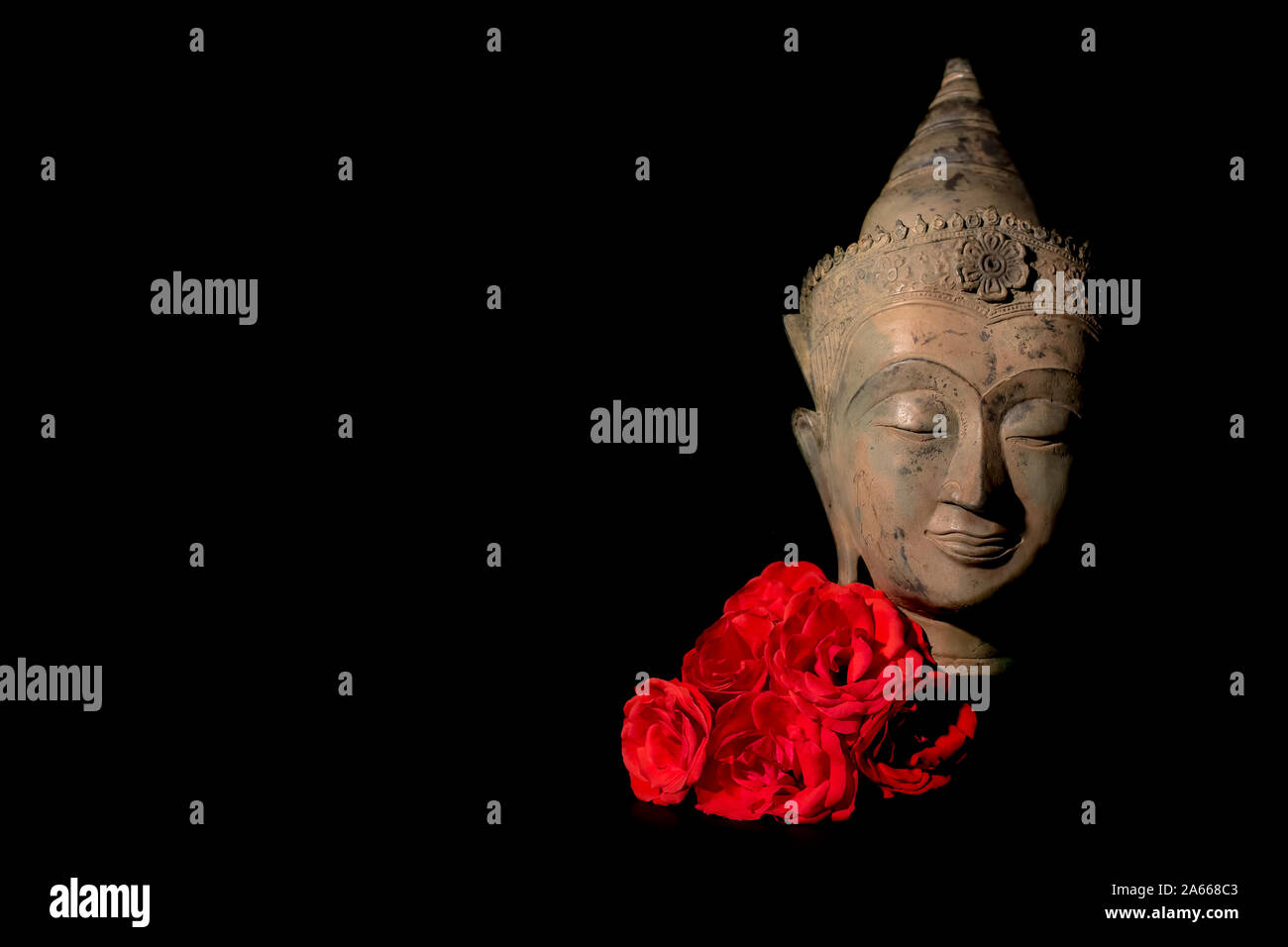 Frieden und Liebe. Serene traditionelle Buddha Kopf Statue mit tief roten Rosen. Die Suche nach spiritueller Erleuchtung durch Meditation. Zen Buddhismus Reinheit und min. Stockfoto