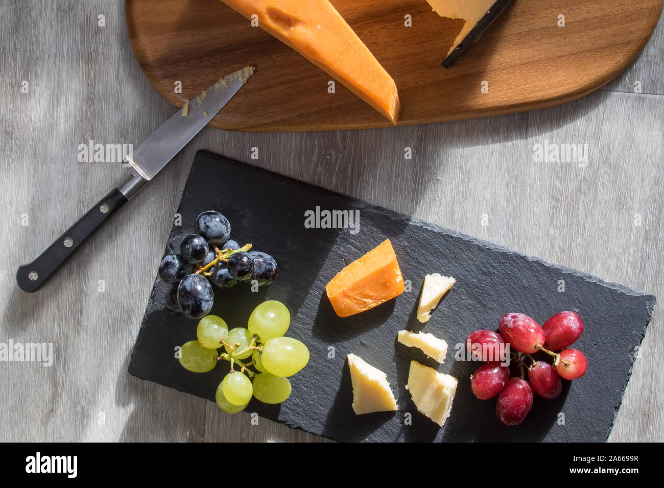 Käse serviert mit Rot weißen und schwarzen Trauben. Flatlay Snack food Bild. Leicester und Cheddar Hartkäse mit Obst auf Holz und sl Stockfoto