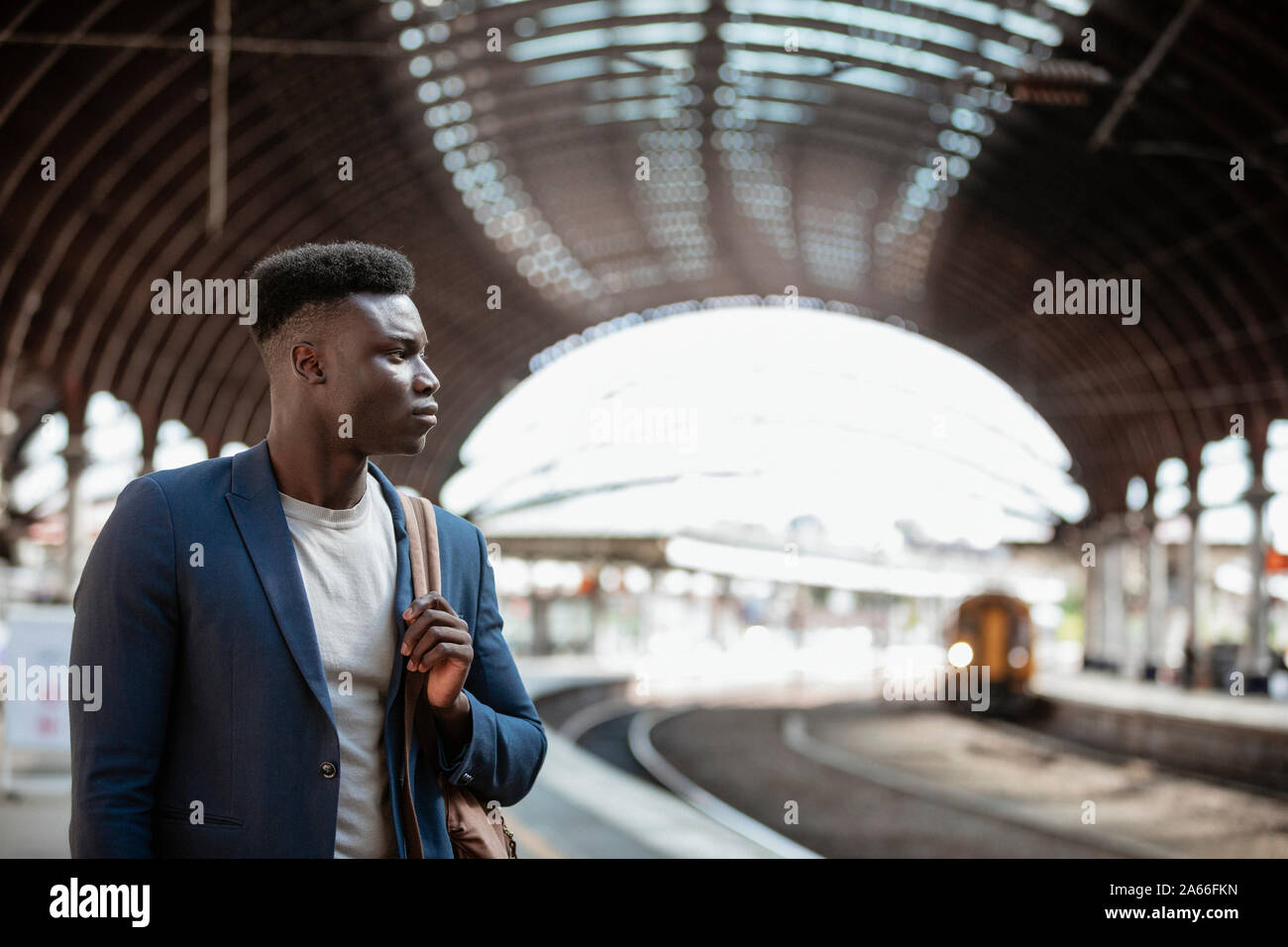 Ein Geschäftsmann warten auf einen Zug auf der Plattform in einem Bahnhof. Er hält einen Rucksack über die Schulter. Stockfoto