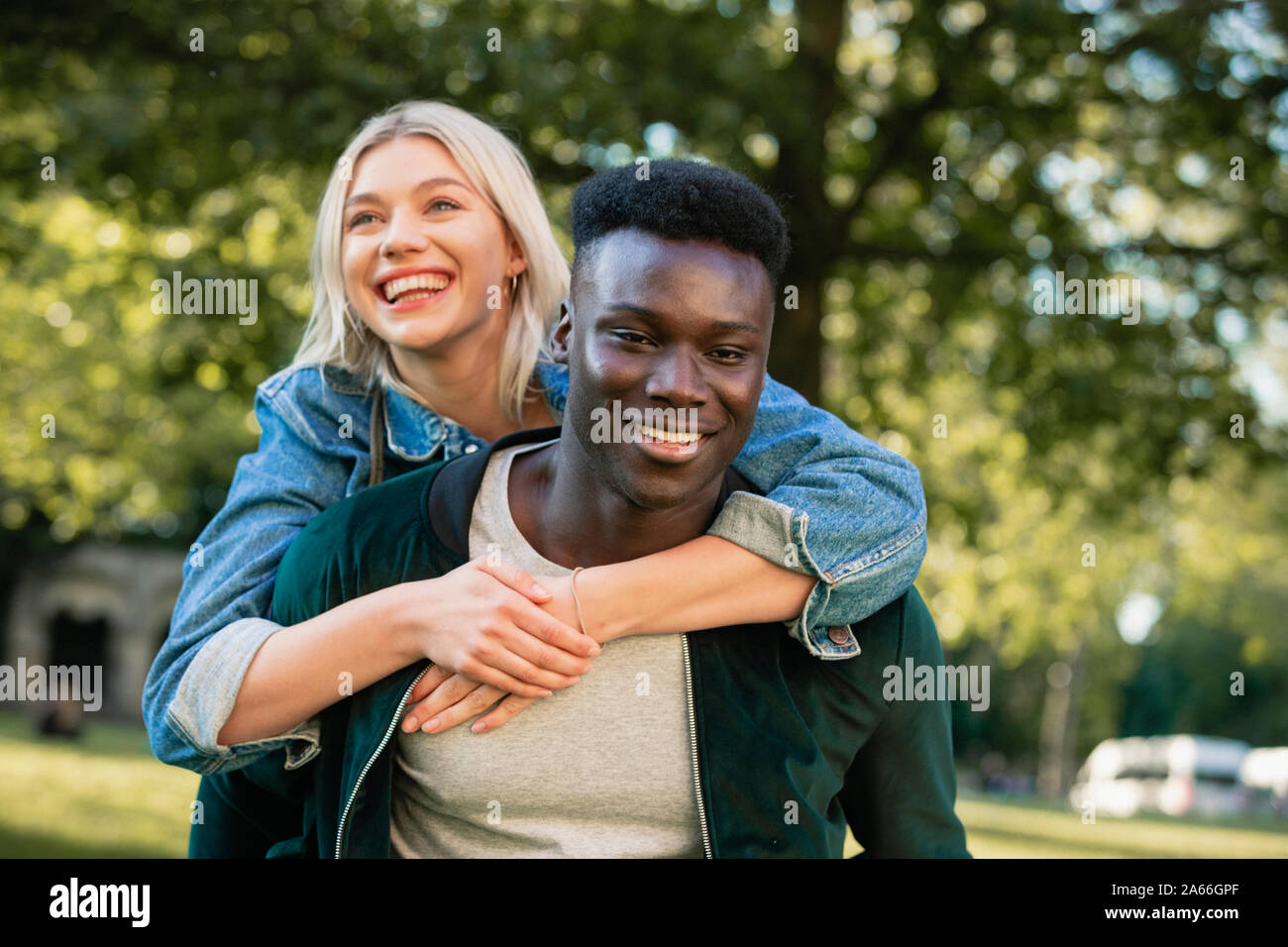 Eine Nahaufnahme von einem Mann, der eine Frau ein Huckepack heben durch einen Park. Sie sind beide lächelnd. Stockfoto