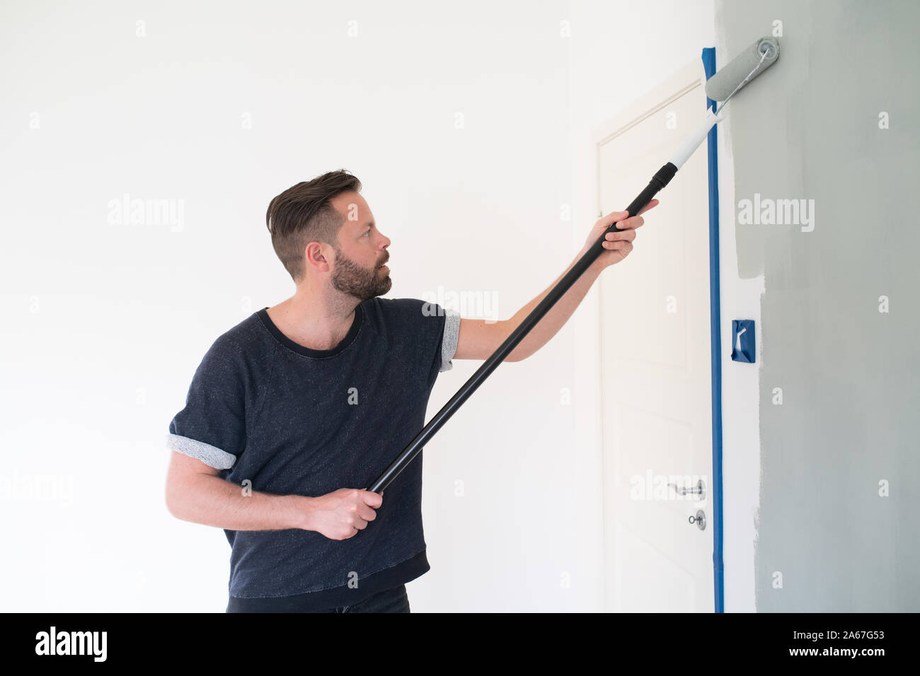 Mann rolling hellgrau Farbe auf Wand Stockfoto