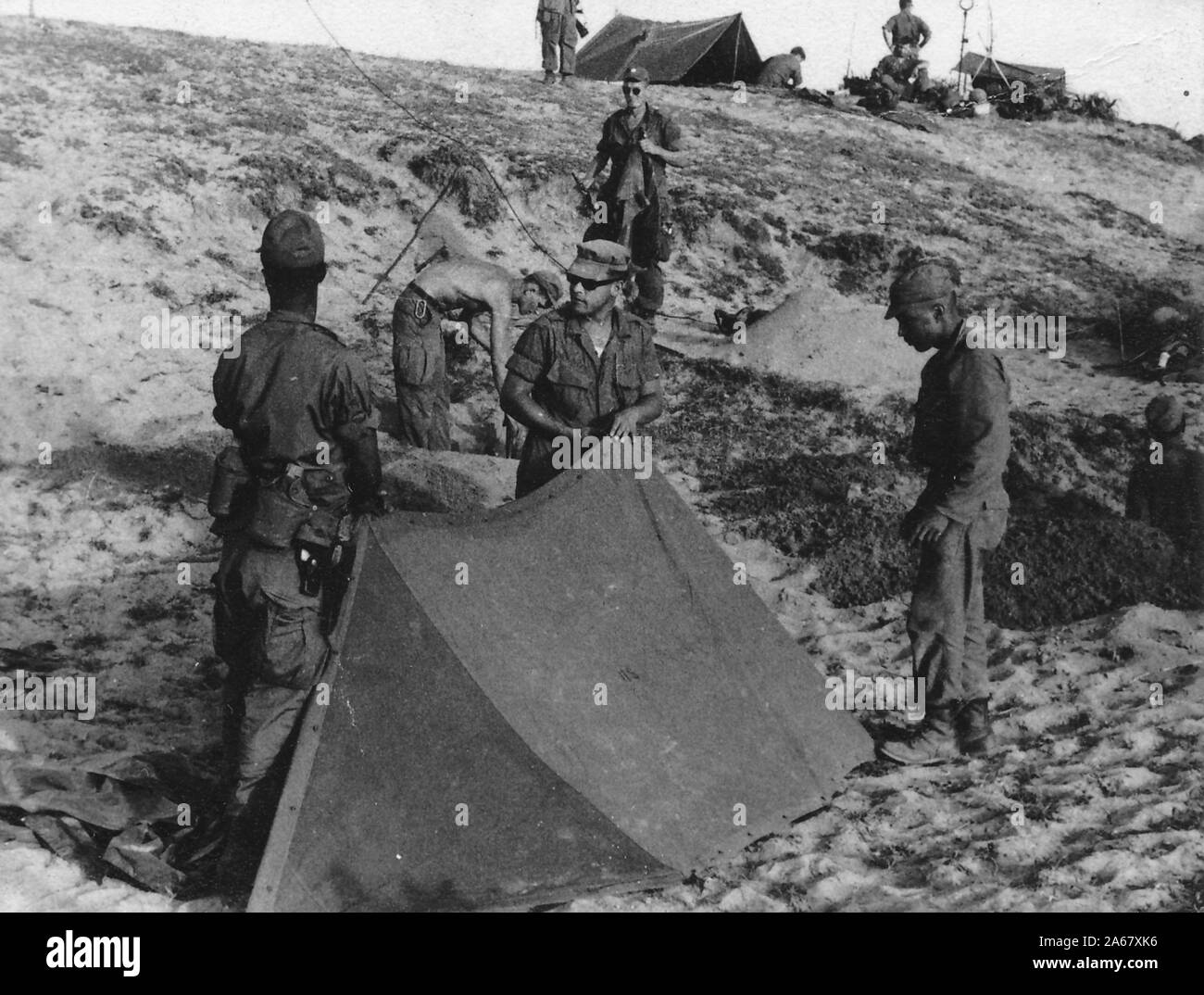 Eine Gruppe amerikanischer Soldaten, draußen an einem sonnigen Tag, die Vorbereitungen für ein Camp auf einem offenen Hügel, Vietnam, 1965 treffen. () Stockfoto