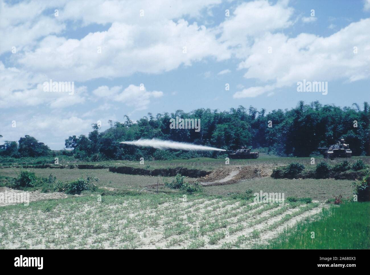 Weitschuss von zwei gepanzerten Fahrzeugen über offene grüne Felder an einem sonnigen Tag, einer schoss eine Rakete in Richtung des Randes einer Waldfläche, Vietnam, 1965. () Stockfoto Weitschuss von zwei gepanzerten Fahrzeugen über offene grüne Felder an einem sonnigen Tag, einer schoss eine Rakete in Richtung des Randes einer Waldfläche, Vietnam, 1965. () Stockfoto