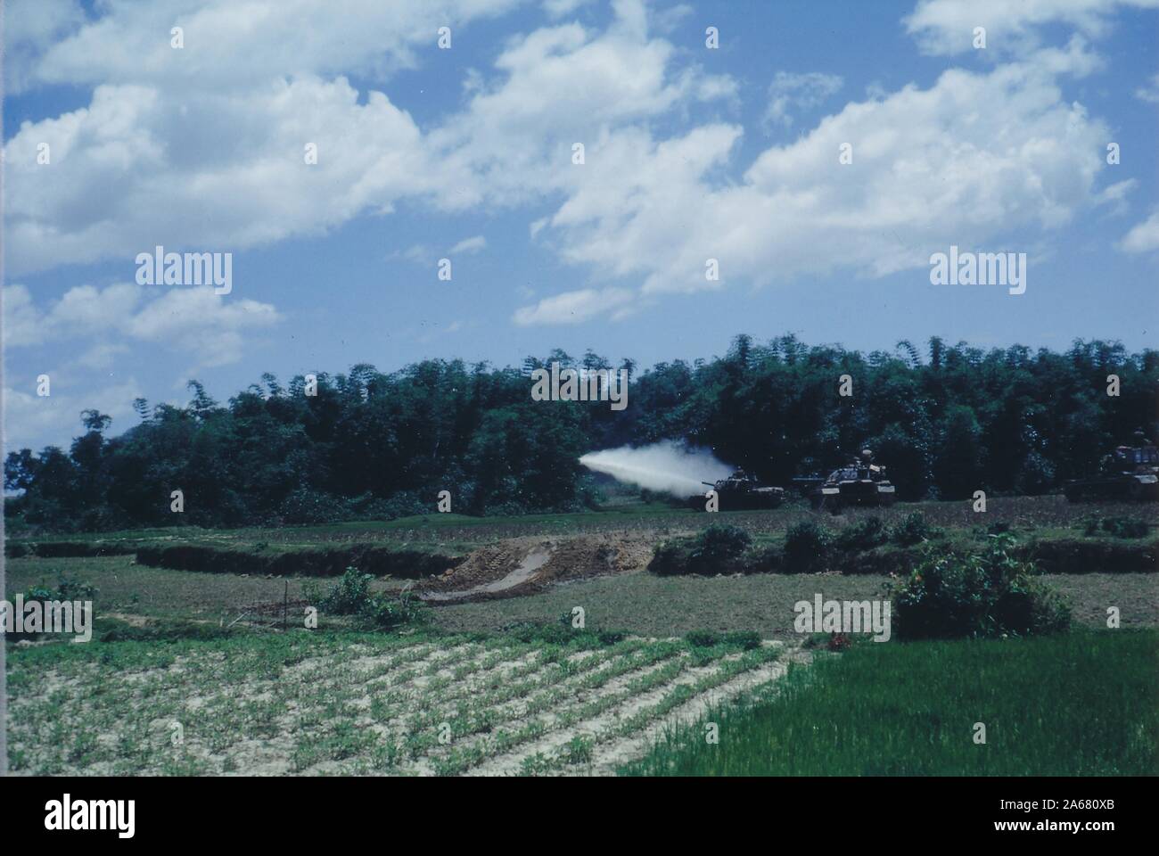 Breiter Schuss, über offene Grünfelder an einem sonnigen Tag, von mehreren gepanzerten Fahrzeugen, einer schoss eine Rakete oder andere Munition in Richtung des Randes einer Waldfläche, Vietnam, 1965. () Stockfoto Breiter Schuss, über offene Grünfelder an einem sonnigen Tag, von mehreren gepanzerten Fahrzeugen, einer schoss eine Rakete oder andere Munition in Richtung des Randes einer Waldfläche, Vietnam, 1965. () Stockfoto