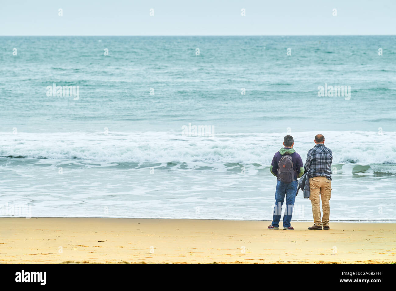 Zwei Männer im mittleren Alter stand in der Kontemplation auf der Küstenlinie von einem Sandstrand neben dem Englischen Kanal in Bournemouth, England. Stockfoto