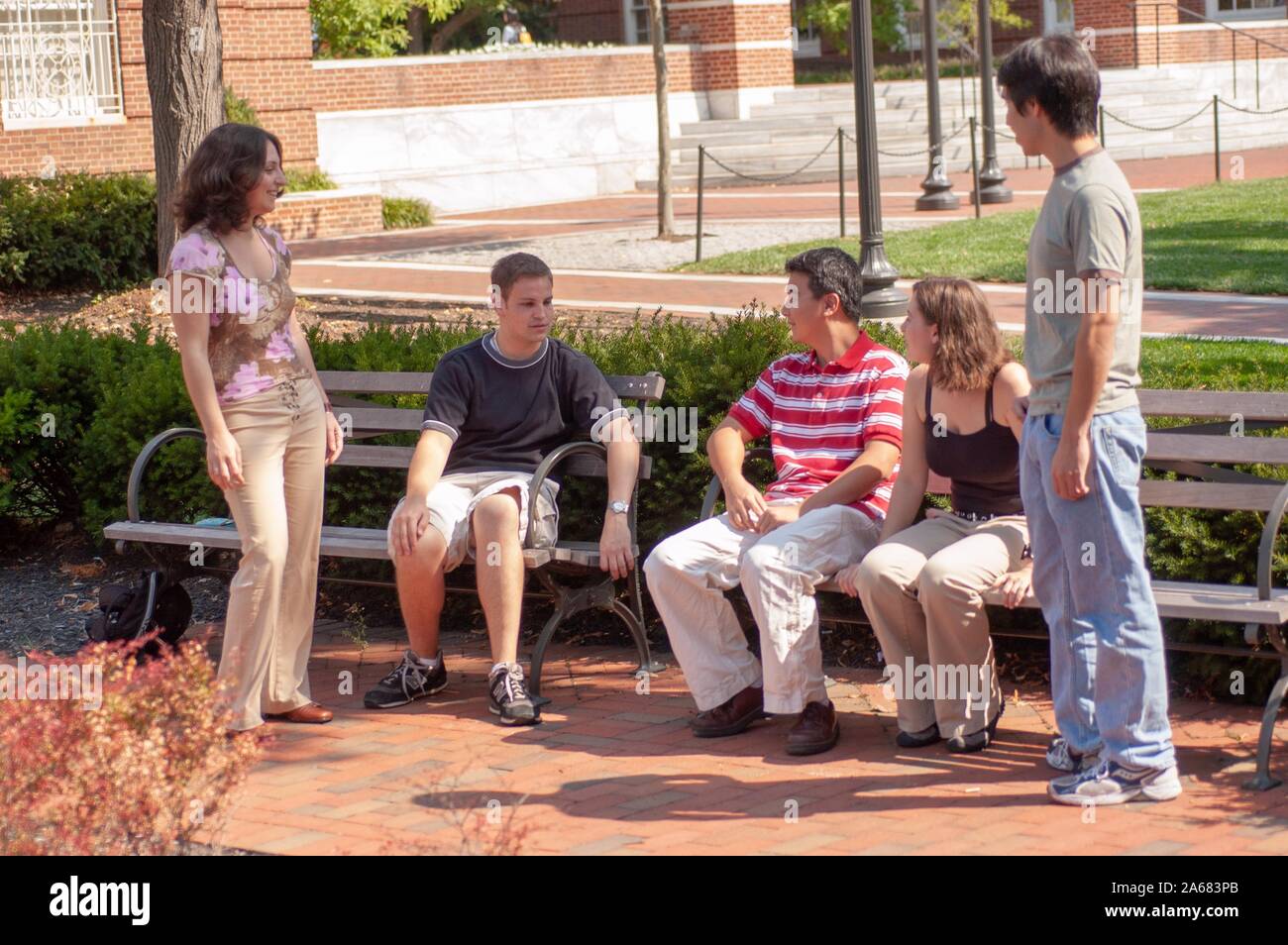 Studenten, die an einem sonnigen Tag draußen auf dem Gelände der Johns Hopkins University, Baltimore, Maryland, sitzen und in der Nähe von Sitzbänken stehen. Aus der Homewood Photography Collection. () Stockfoto