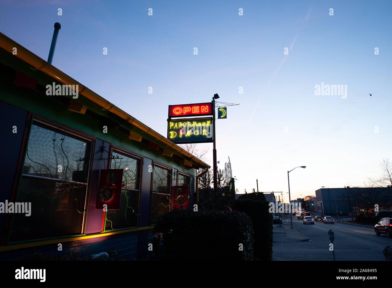 Am Abend wurde ein wenig abgewinkelter Schuss von Autos auf einer Straße neben einem Gebäude mit einer Neon-Schild gedreht, die den Papermoon Diner, Baltimore, Maryland, am 8. Januar 2008 wirbt. Aus der Homewood Photography Collection. () Stockfoto