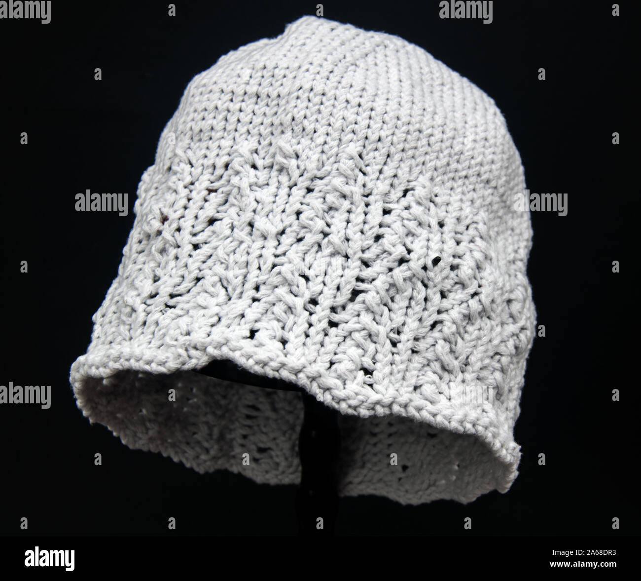 Hellgrau gestrickt hat Fashion Accessoire für Winter auf einem schwarzen Hintergrund. Fibre kunst Bekleidung craft Objekt mit detaillierten Stiche, Stockfoto