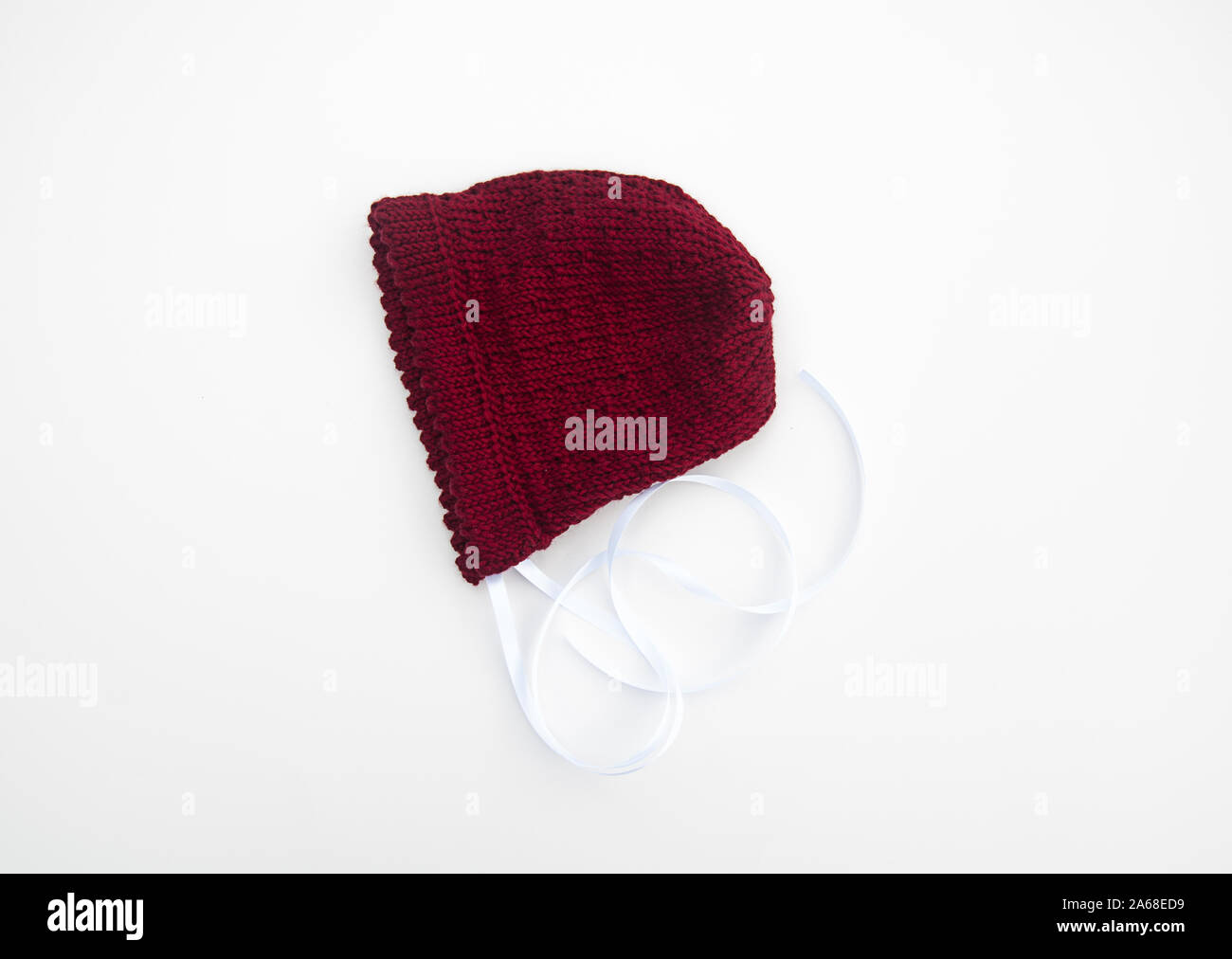 Cranberry rot gefärbt, Baby Mütze Stricken auf hellem Hintergrund isoliert. Baby Hut hat weißen Satinband. Stockfoto