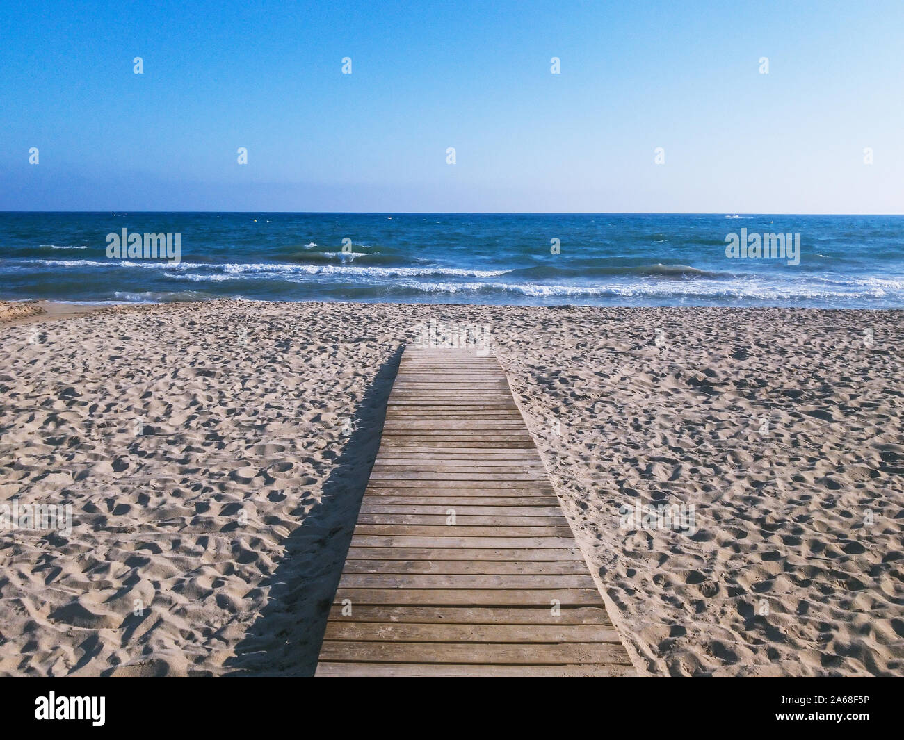 Holz- Pfad zum Wasser an einem Sandstrand am Meer unter blauem Himmel Stockfoto