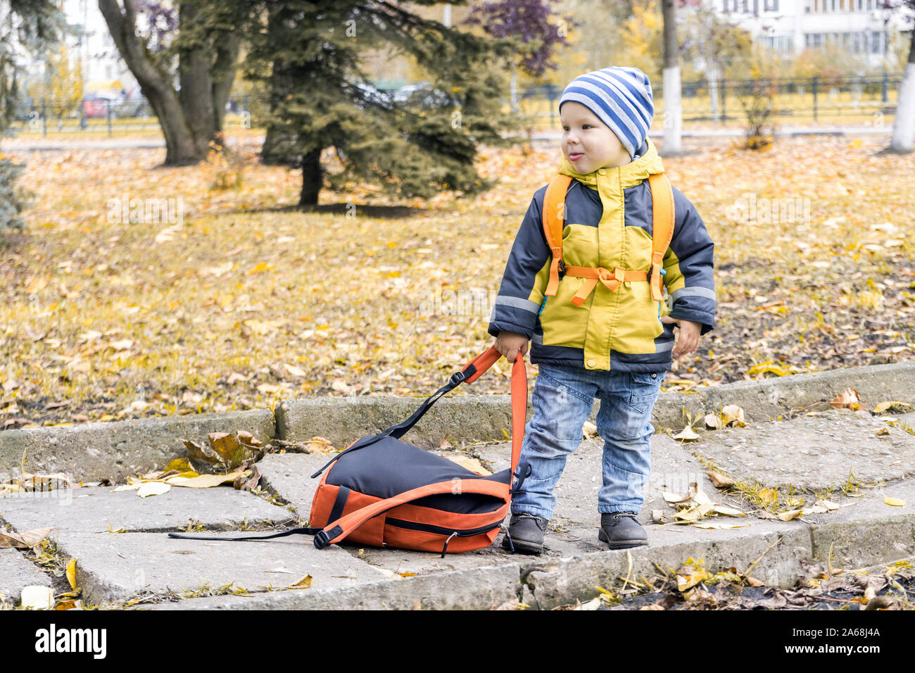 Wenig hooligan Junge gezogen weg Rucksack seiner Mutter und an ihrer im Herbst Stadtpark Grimasse. Stockfoto
