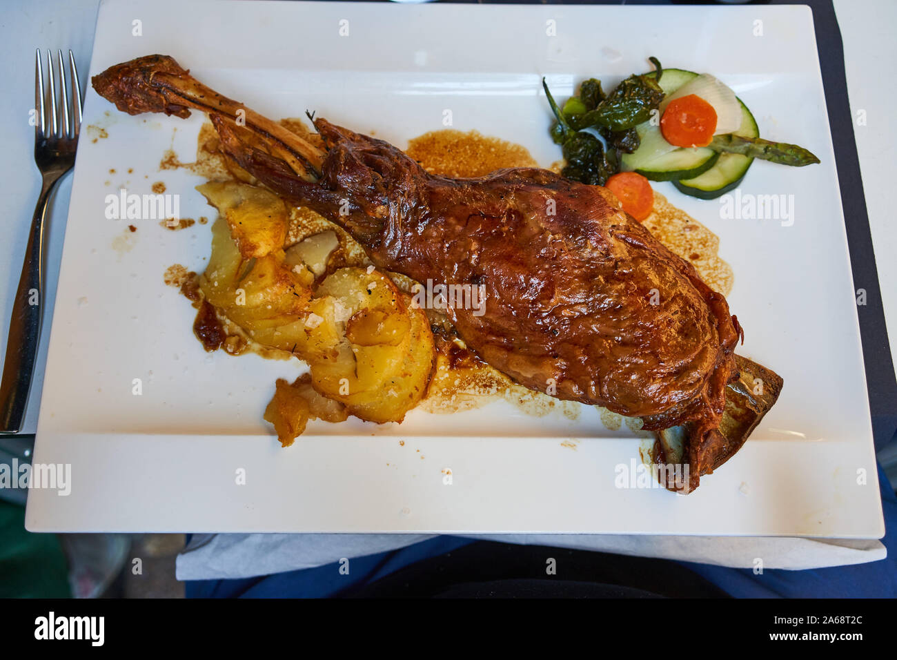Geschmortenes Lammkeule mit geschnittenen Kartoffeln und einem Beilagensalat auf einem quadratischen Teller auf der Terrasse des Restaurante Palomeque, Zaragoza Stockfoto