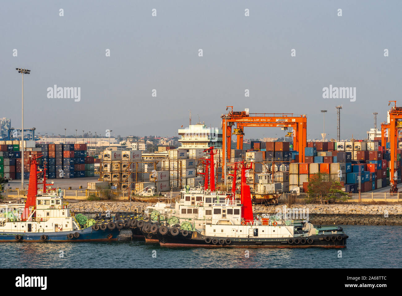 Laem Chabang Seehafen, Thailand - 17. März 2019: Reihen von verankert Schlepper vor Container Yard mit Stapeln und orange Transporter wie Brücken Stockfoto