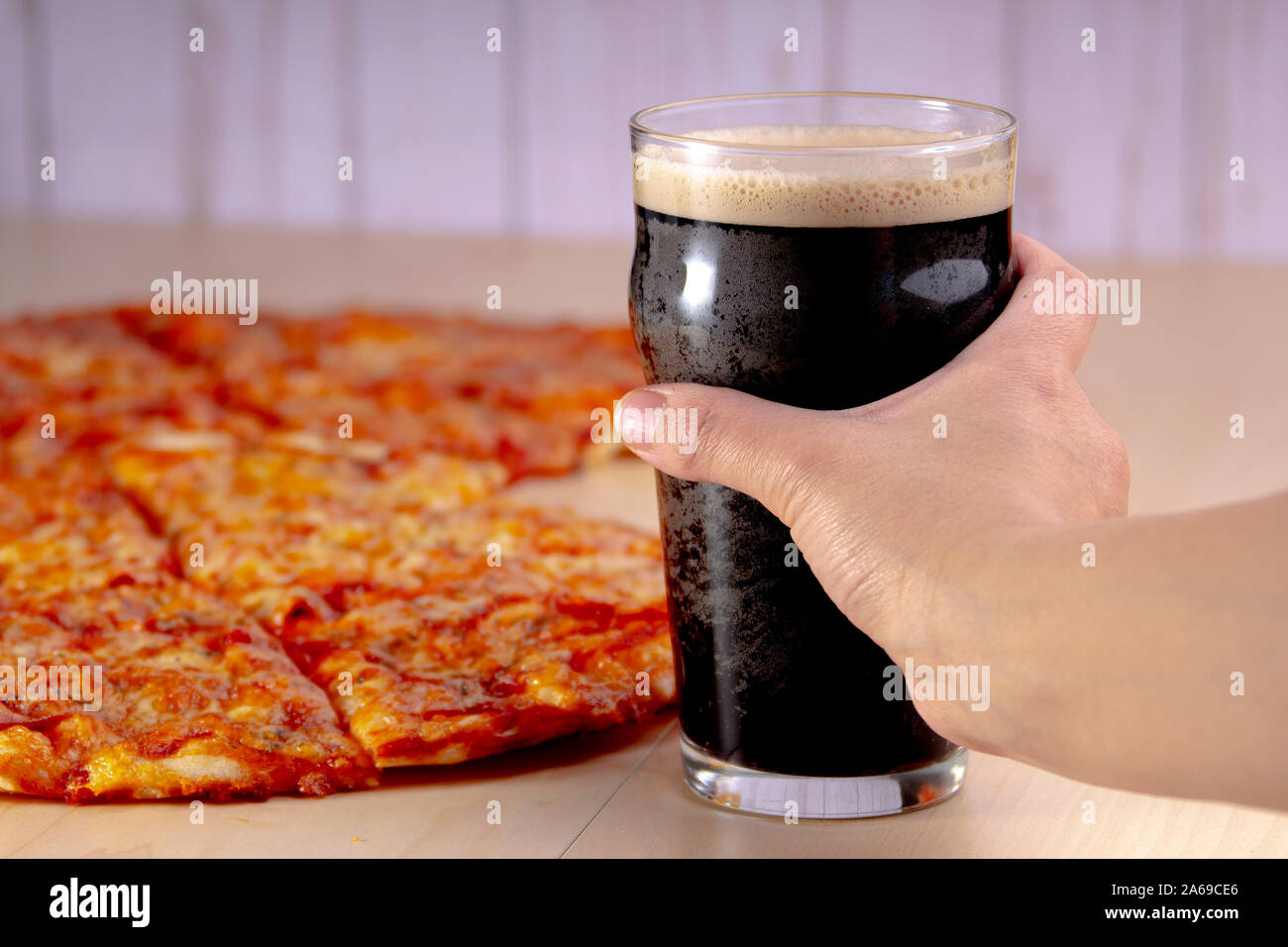 Person ein dunkles Bier mit Pizza halten Stockfoto