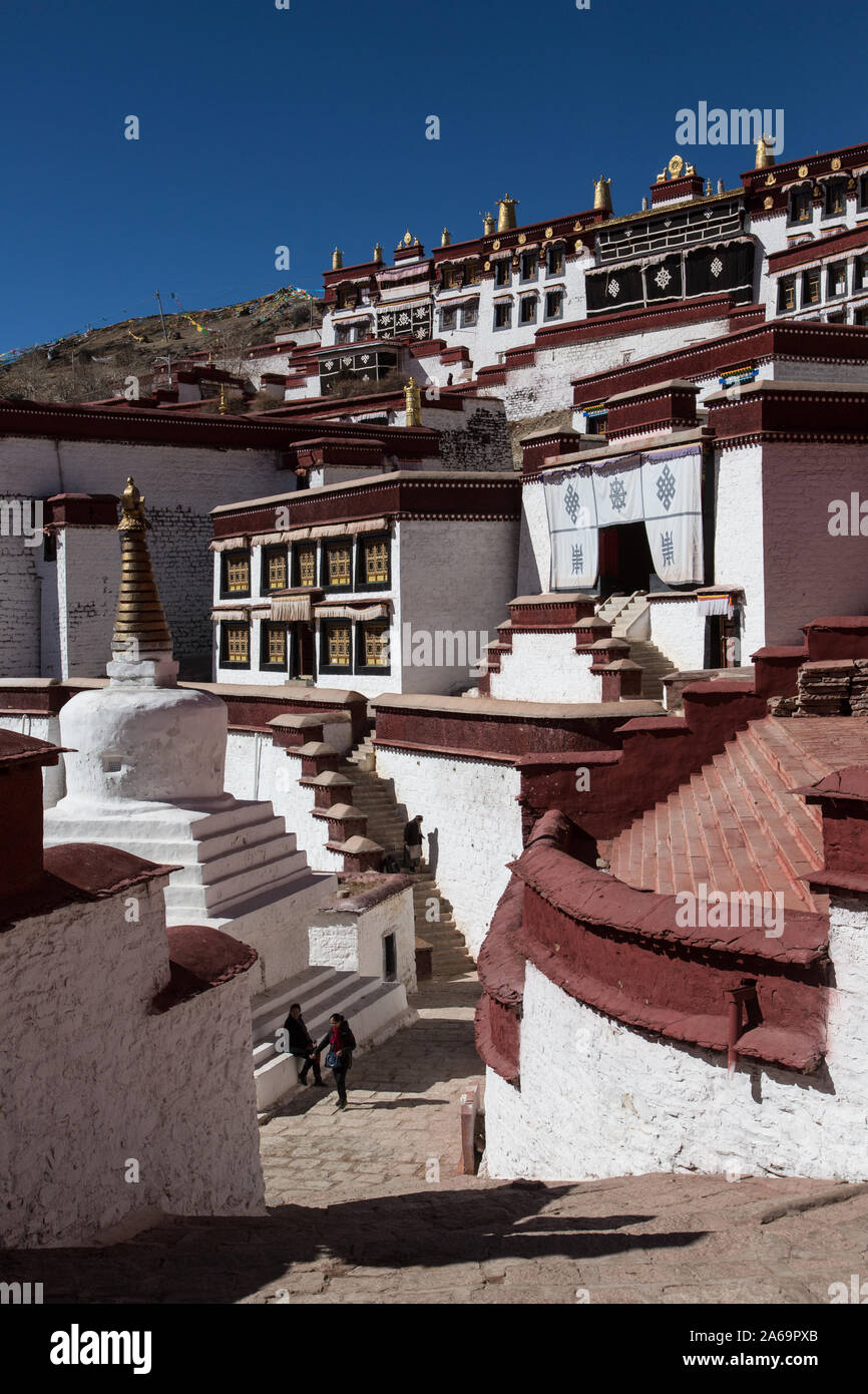 Zwei Besucher durch eine Stupa in den Ganden BuddhistMonastery auf Wangbur Mountain in Tibet als ältere tibetische Frau steigt einige Treppen. Stockfoto