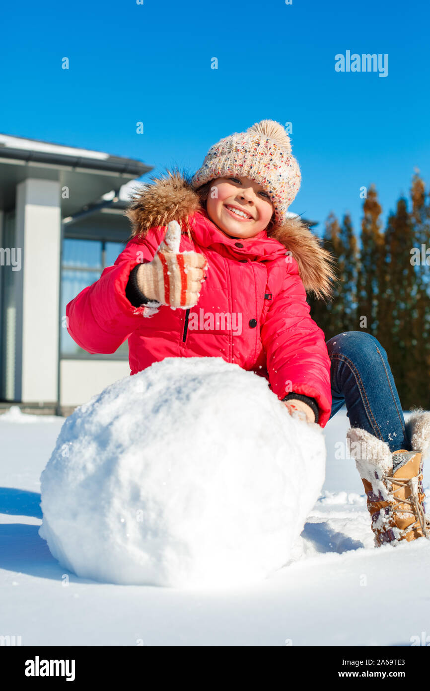 Winter Urlaub. Stehendes Mädchen im Freien in der Nähe von Haus saß rollenden Schneeball für Schneemann lächelt Fröhlich close-up Stockfoto