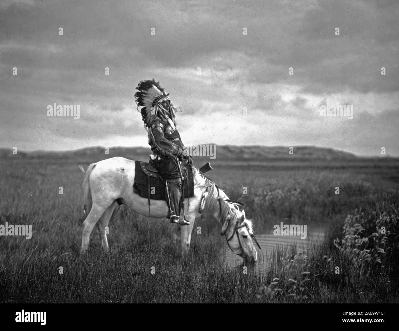 Edward S. Curtis Native American Indians - Red Hawk, ein oglala Krieger, sitzend auf einem Pferd, das Trinkwasser wird aus einem kleinen Teich in den Badlands Ca. 1905 Stockfoto